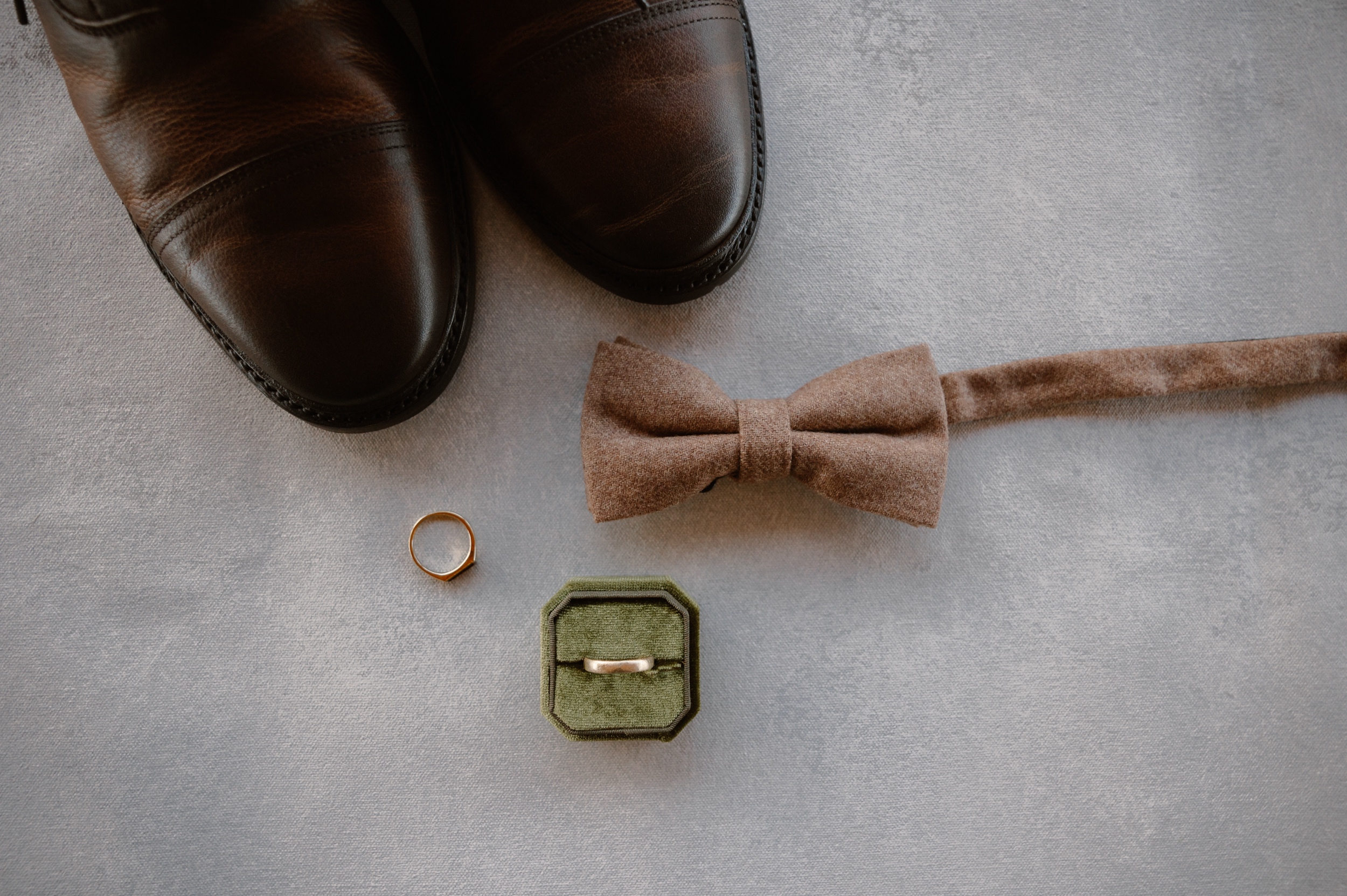 A color photo of a groom's shoes, bowtie, and wedding rings laid on a solid background. Photo by Ashley Joyce.