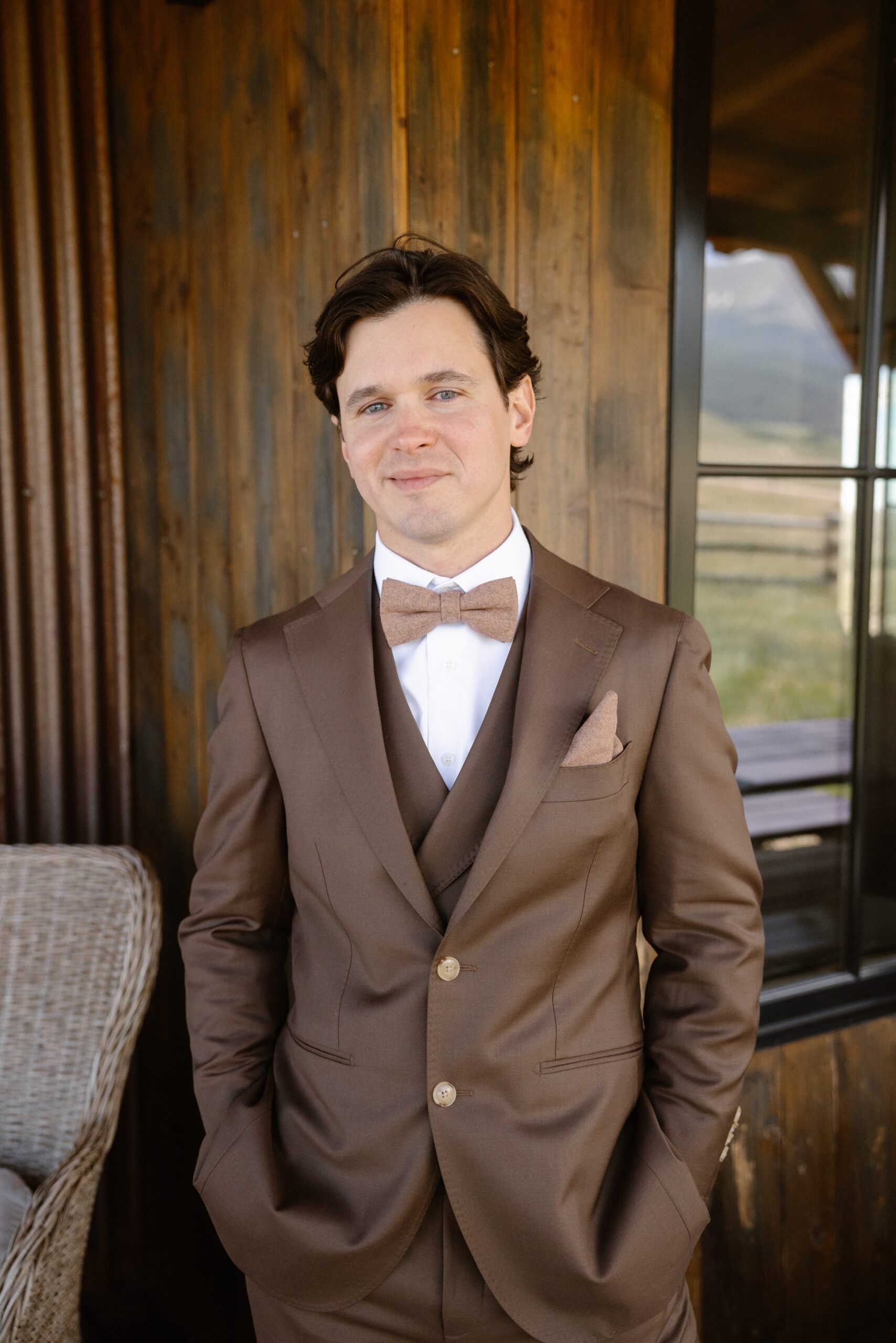 A photo of a groom standing on the patio at Three Peaks Ranch with his hands in his pockets. Photo by Colorado wedding photographer Ashley Joyce.