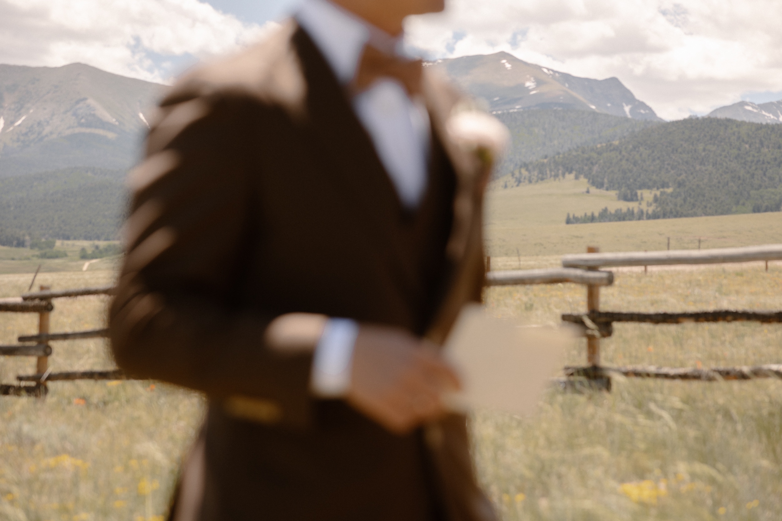 A blurry photo of a groom standing in a grass field while he waits for his fiance to arrive for their first look. Photo by Colorado wedding photographer Ashley Joyce.