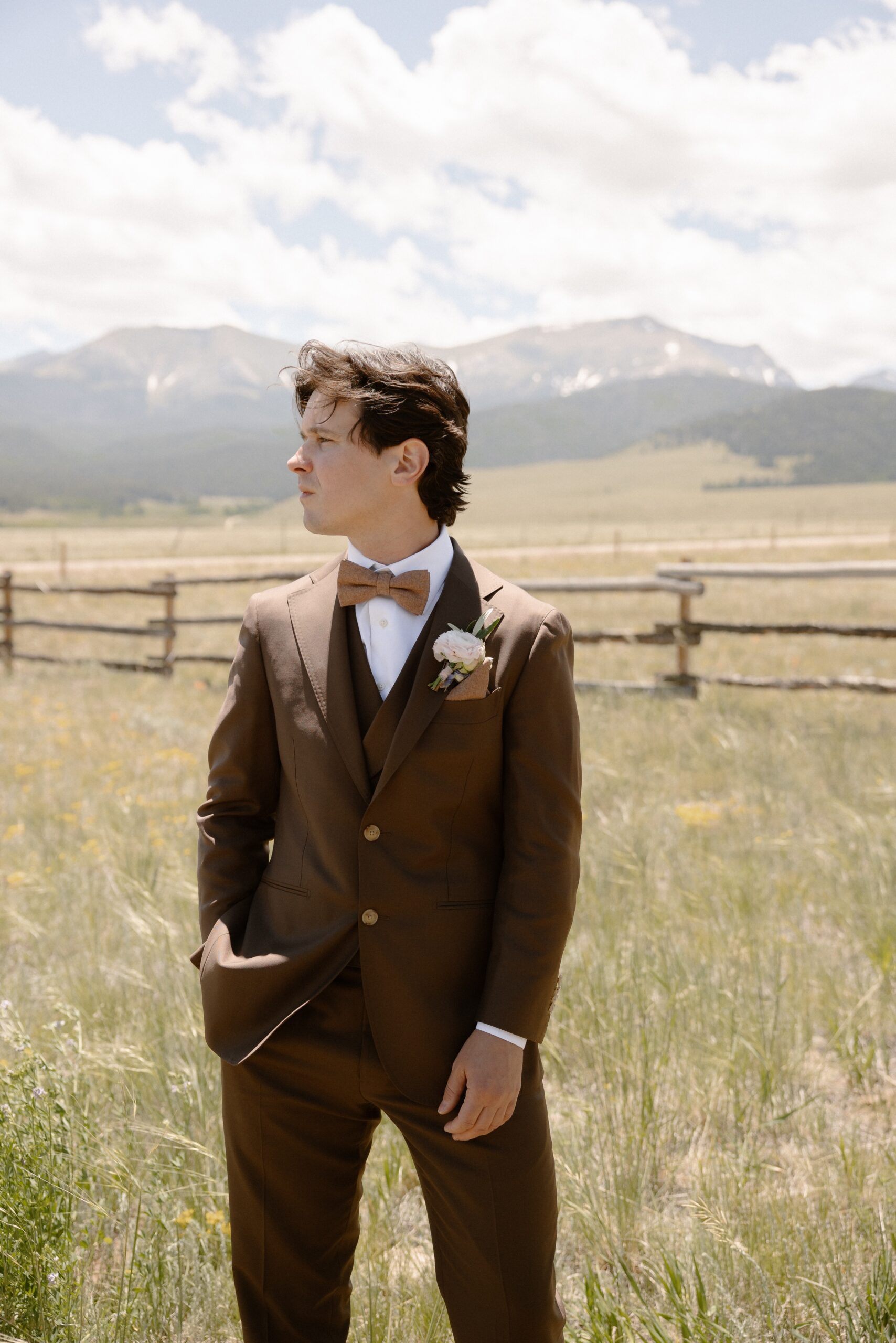 A photo of a groom standing in a sunny grass field for his groom portraits before his Three Peaks Ranch wedding. Photo by Colorado wedding photographer Ashley Joyce.