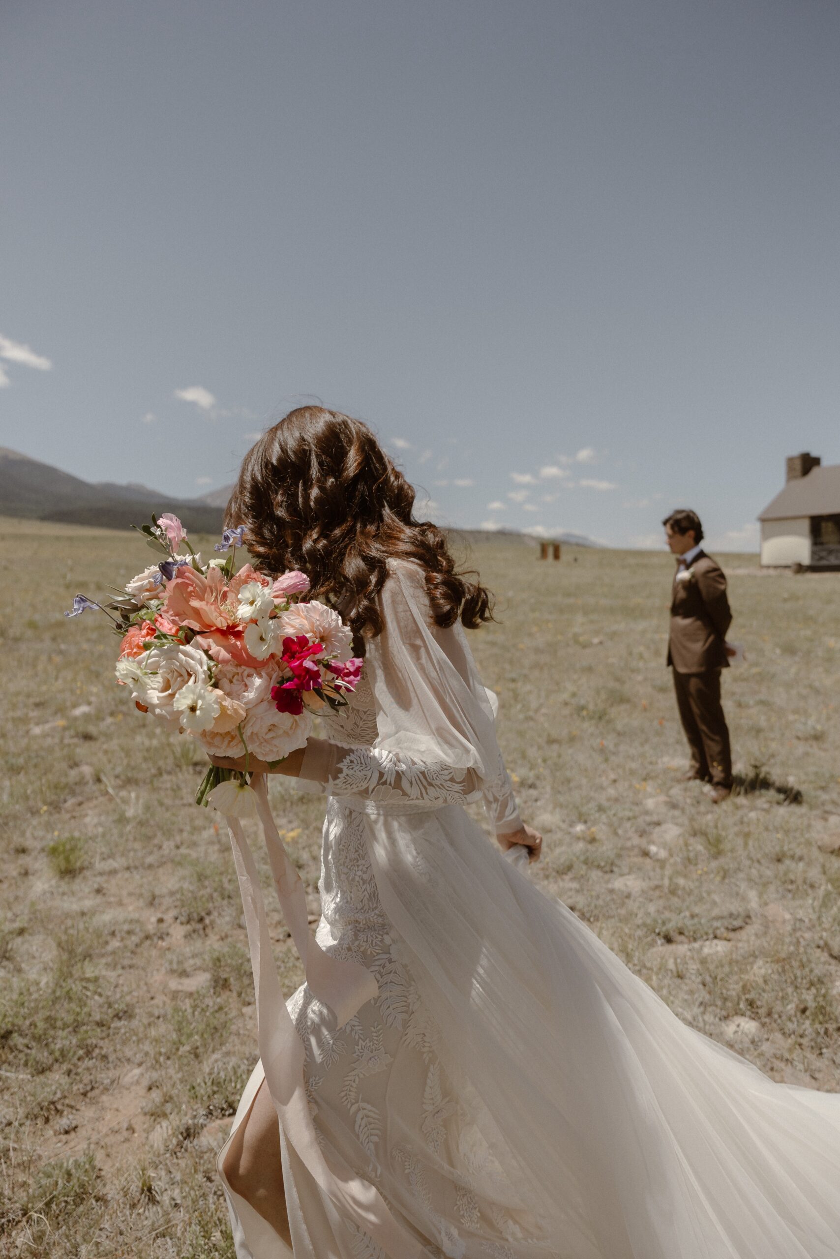 A bride walks through a grassy field at Three Peaks Ranch while she gets ready for her first look with her soon-to-be-husband. Photo by Colorado wedding photographer Ashley Joyce.