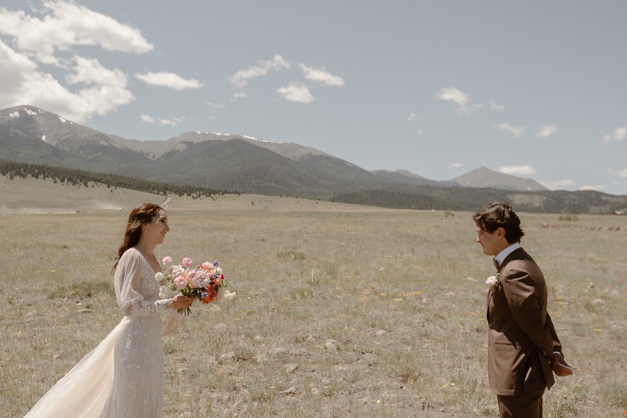 A bride and groom see each other for the first time while they stand in a grassy field at Three Peaks Ranch. Photo by Colorado wedding photographer Ashley Joyce.