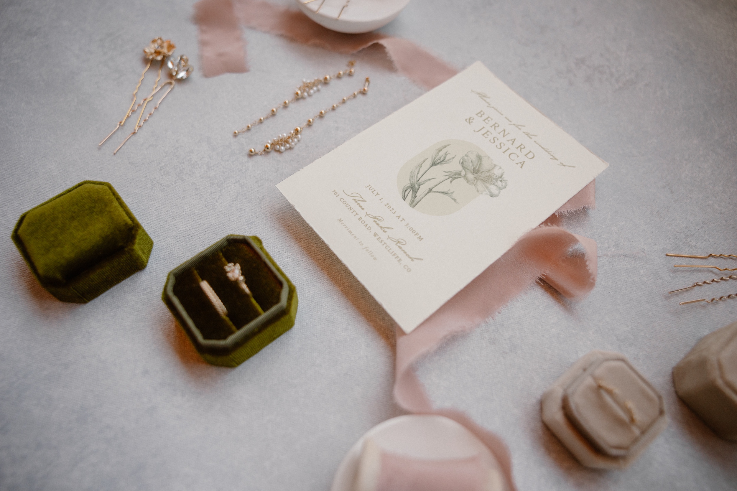 A photo of a couple's wedding details, including their wedding invitation, wedding rings, and accessories. Photo by Ashley Joyce.