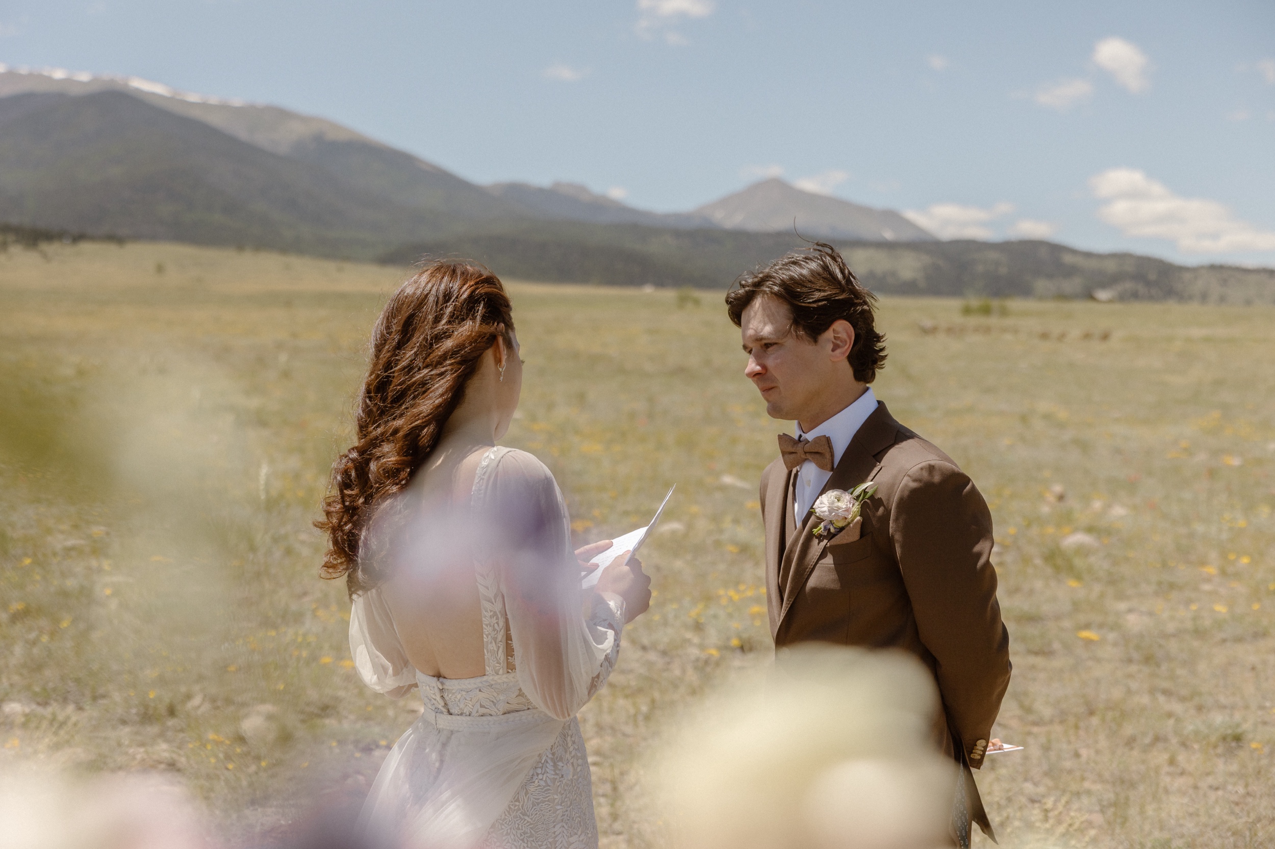 A bride and groom stand in a grassy field as they face each other while they say their private vows to one another before their Three Peaks Ranch wedding in Westcliffe, Colorado. Photo by Colorado wedding photographer Ashley Joyce.