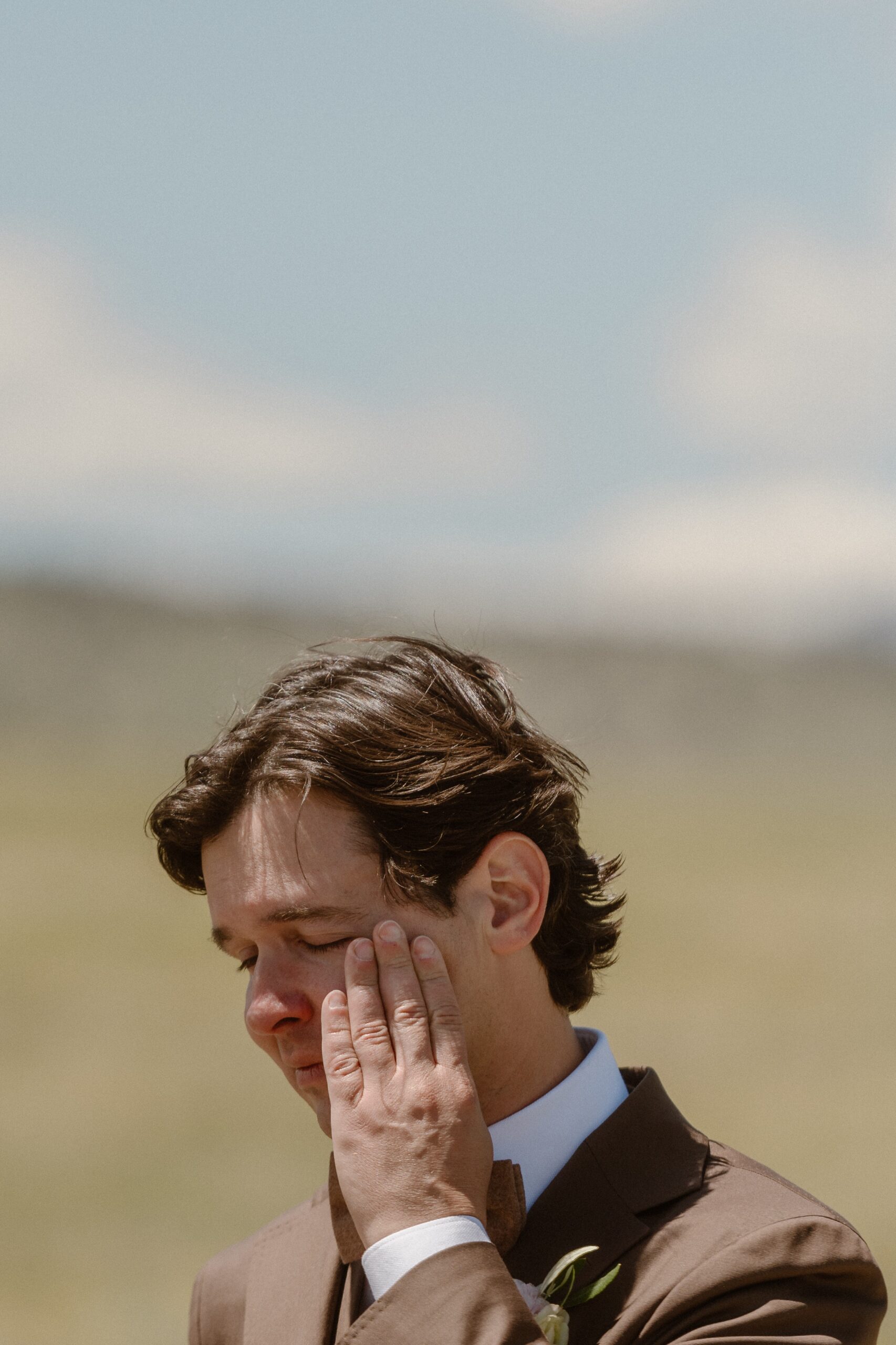 A groom wipes his tears away in a grassy field. Photo by Colorado wedding photographer, Ashley Joyce.