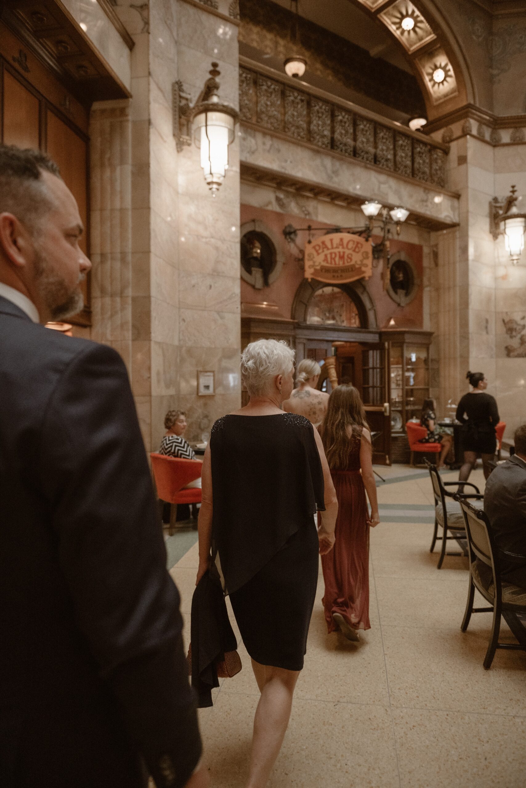 A bride and groom walk into the Brown Palace with their wedding guest for their high tea reception. Photo by Denver wedding photographer Ashley Joyce.