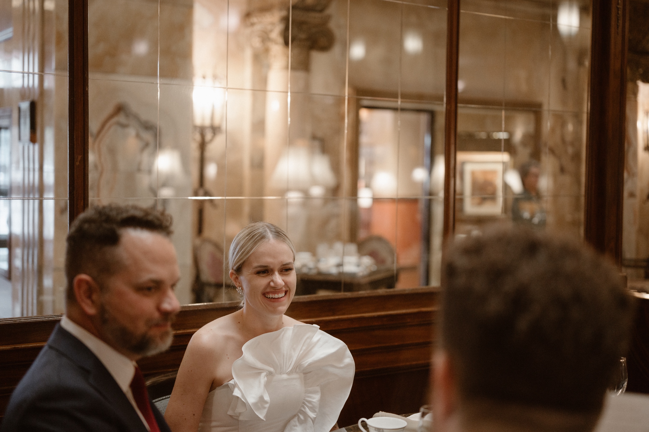 A bride laughs while she sits at her high tea wedding reception at the Brown Palace. Photo by Denver wedding photographer Ashley Joyce.