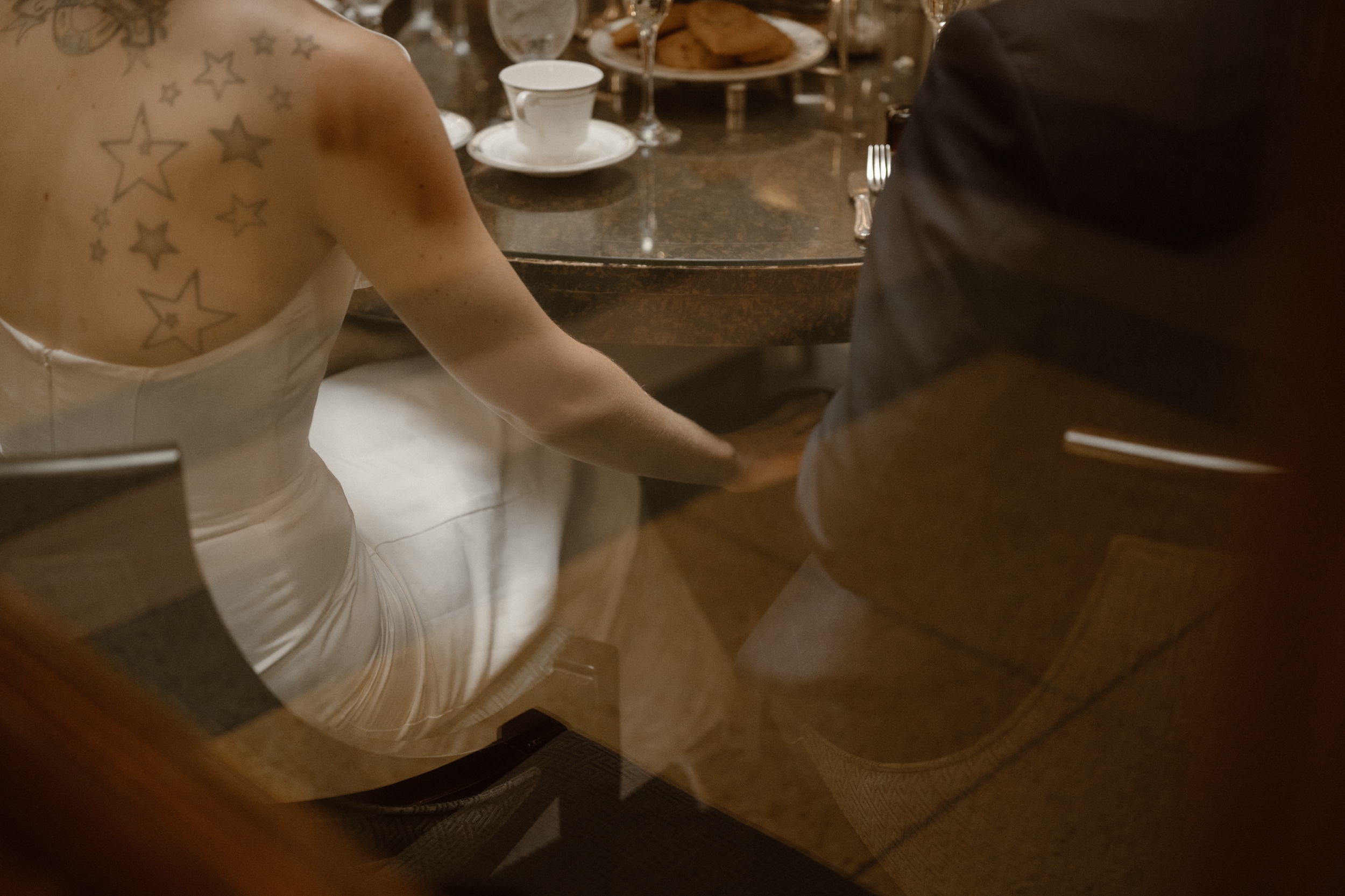 A bride and groom hold hands under the table at their high tea reception at the Brown Palace in Denver, Colorado. Photo by Denver wedding photographer Ashley Joyce.