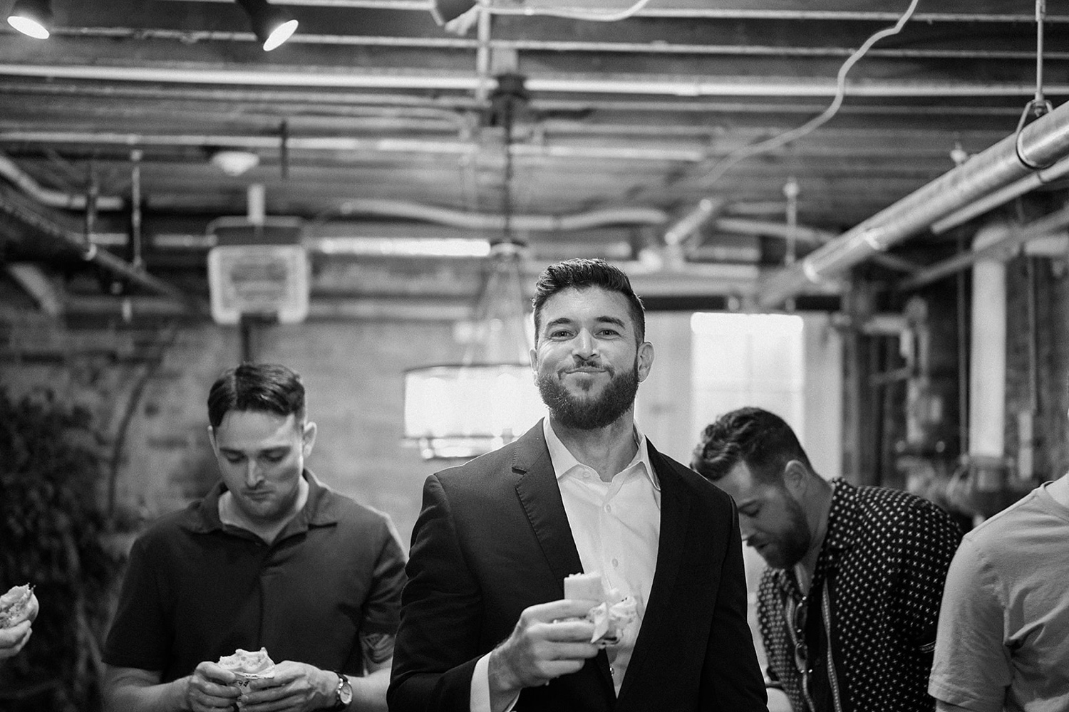 A groom smiling at the camera while he's surrounded by his groomsmen