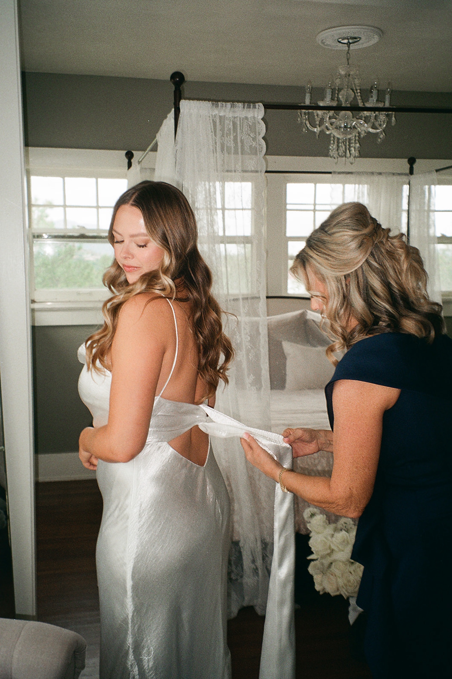 A film photo of a bride getting her wedding dress tied together by her mother at The Manor House