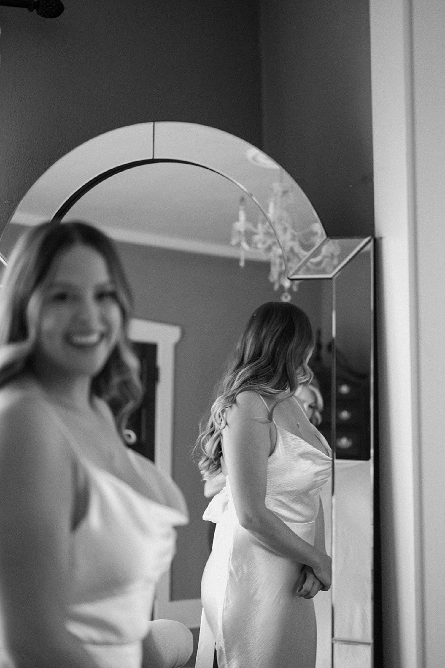 A bride smiling at the camera while her reflection in the background is in focus and she is out of focus