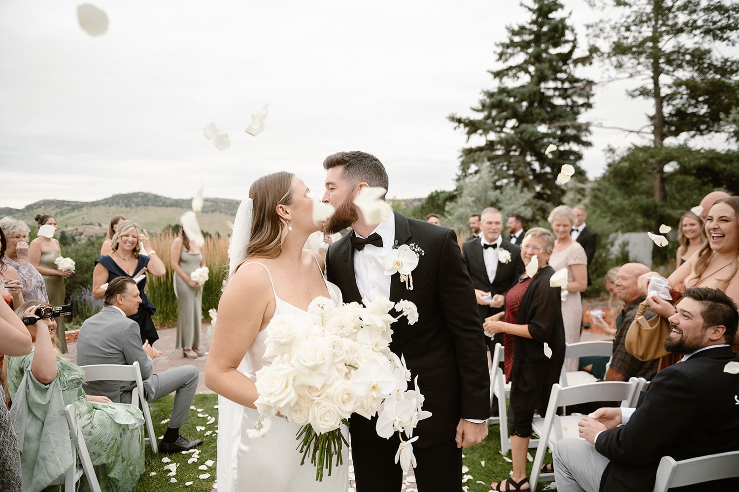 A wedding couple kiss one another while they walk down the aisle after their wedding ceremony