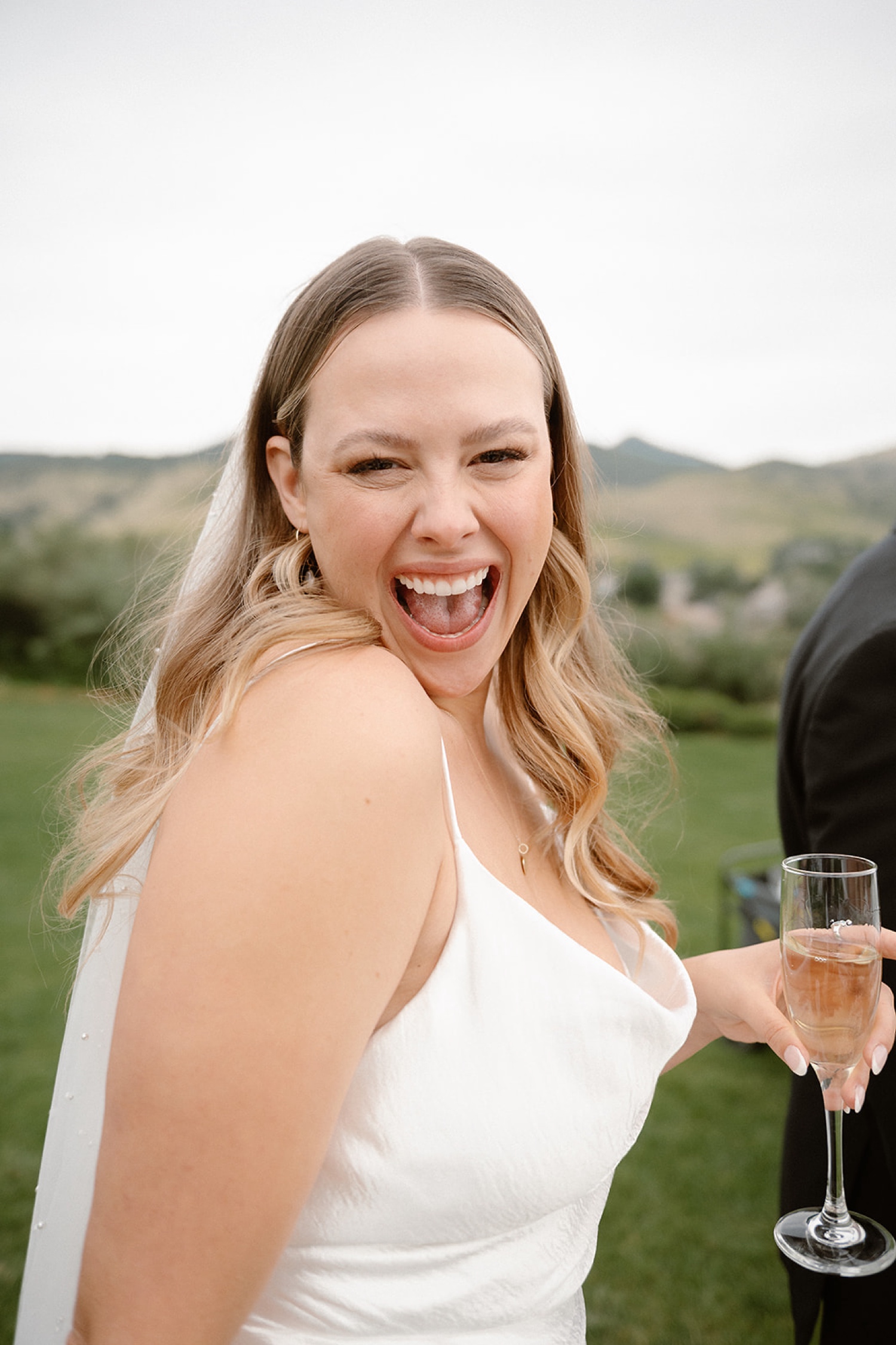 A bride happily smiles at the bride while carrying a glass of champagne