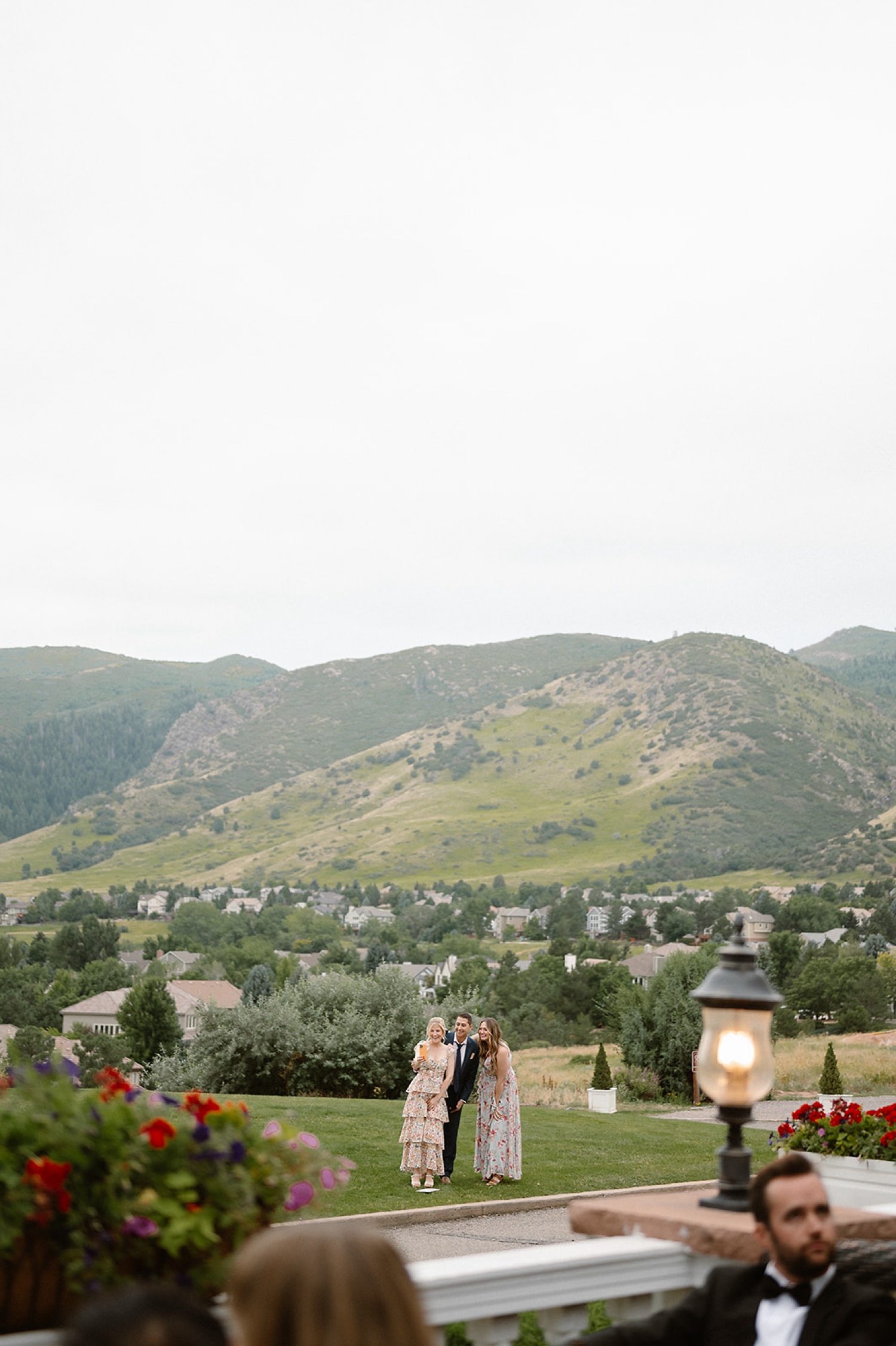 Wedding guests stand in a grass field with mountains in the background