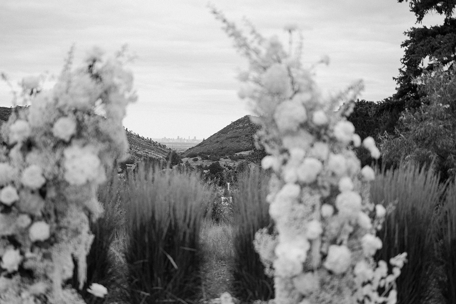 Black and white photo of a wedding arch blurry in the foreground and a city skyline in the background