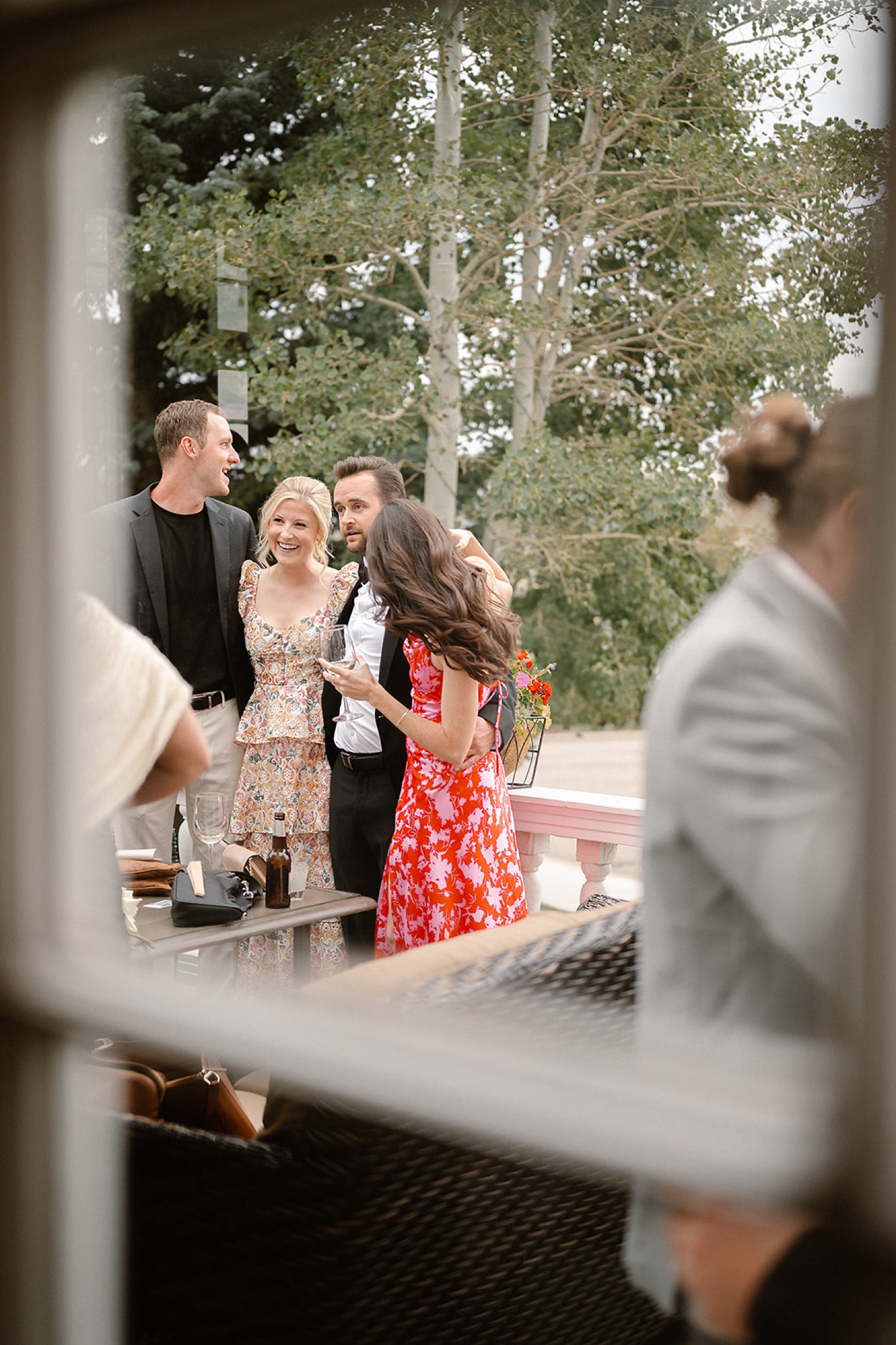 Wedding guests stand and laugh together on the patio during cocktail hour