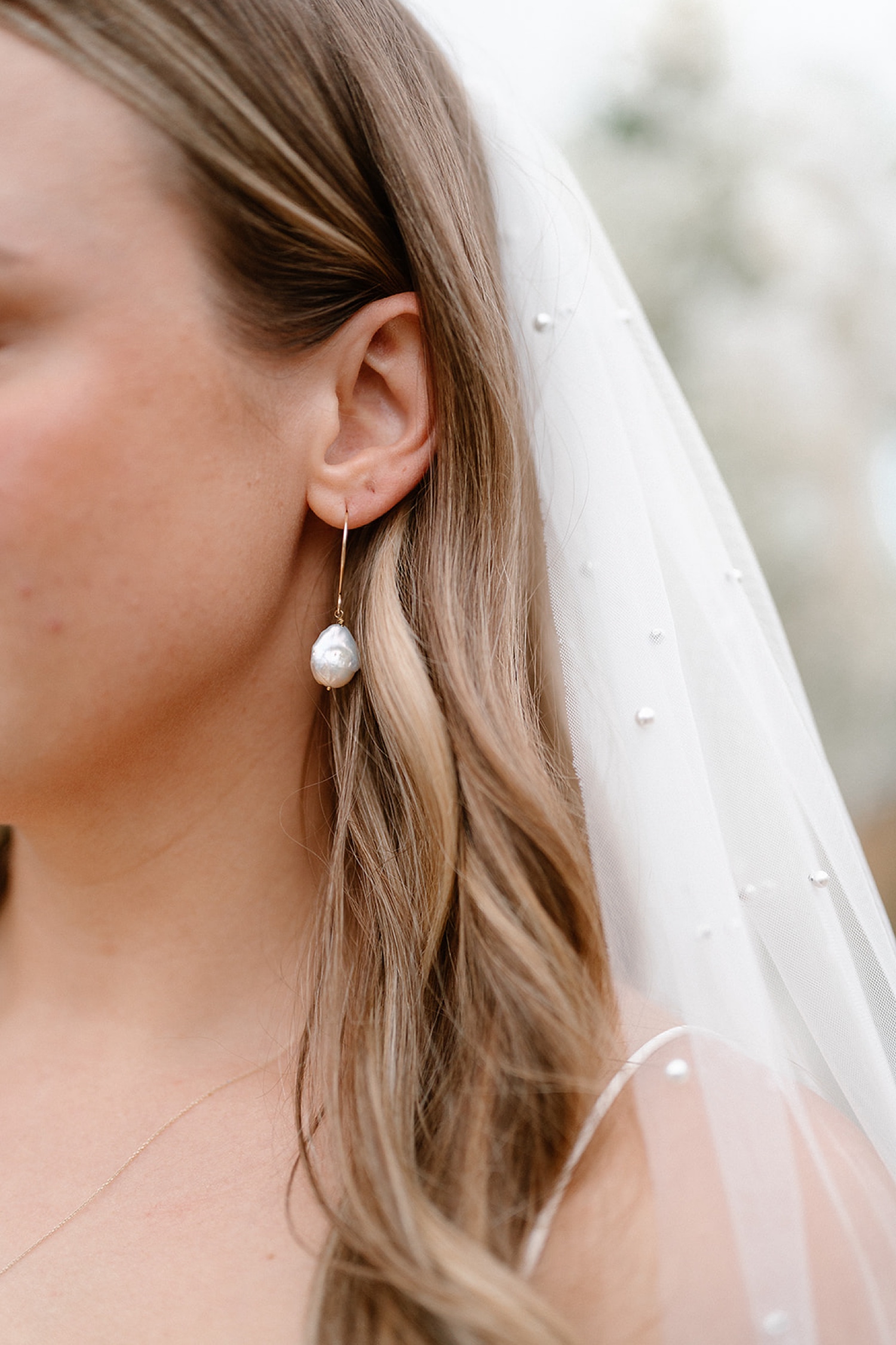 A detail of a bride wearing a pearl earring and a delicate veil with pearls