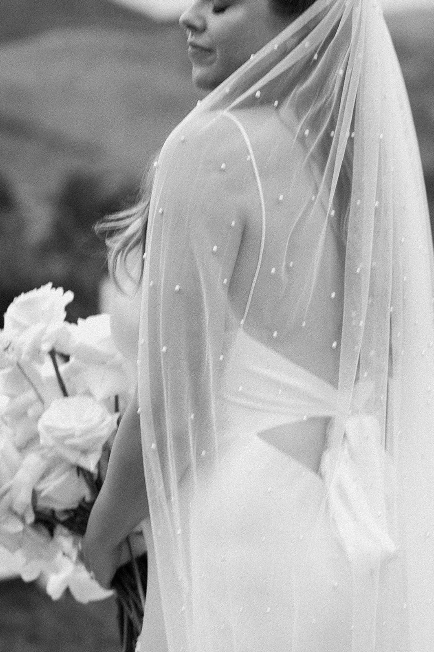 A bride poses for her wedding portraits with a veil covered in pearls covering her