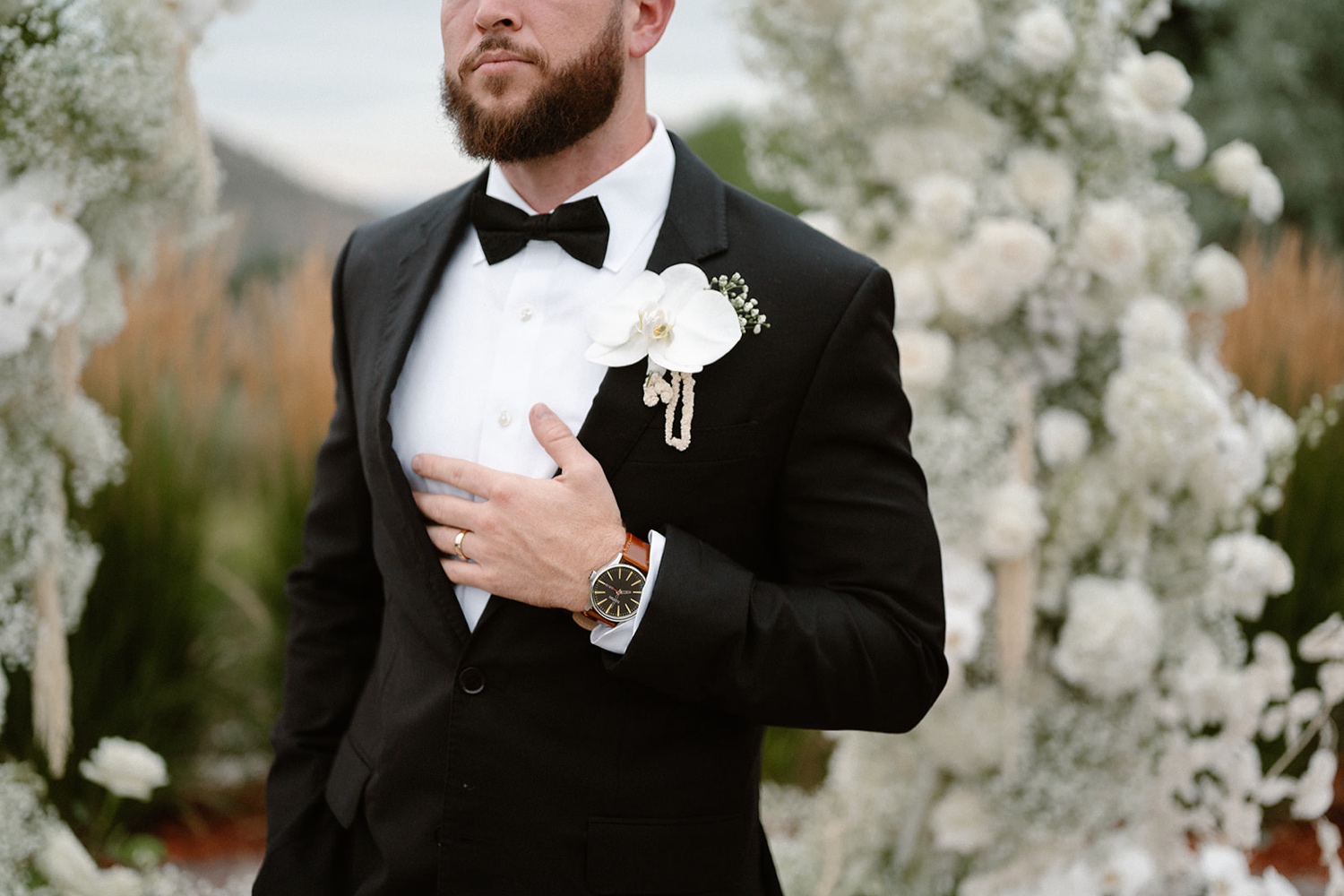 A groom poses with his hand on his chest for his wedding portraits