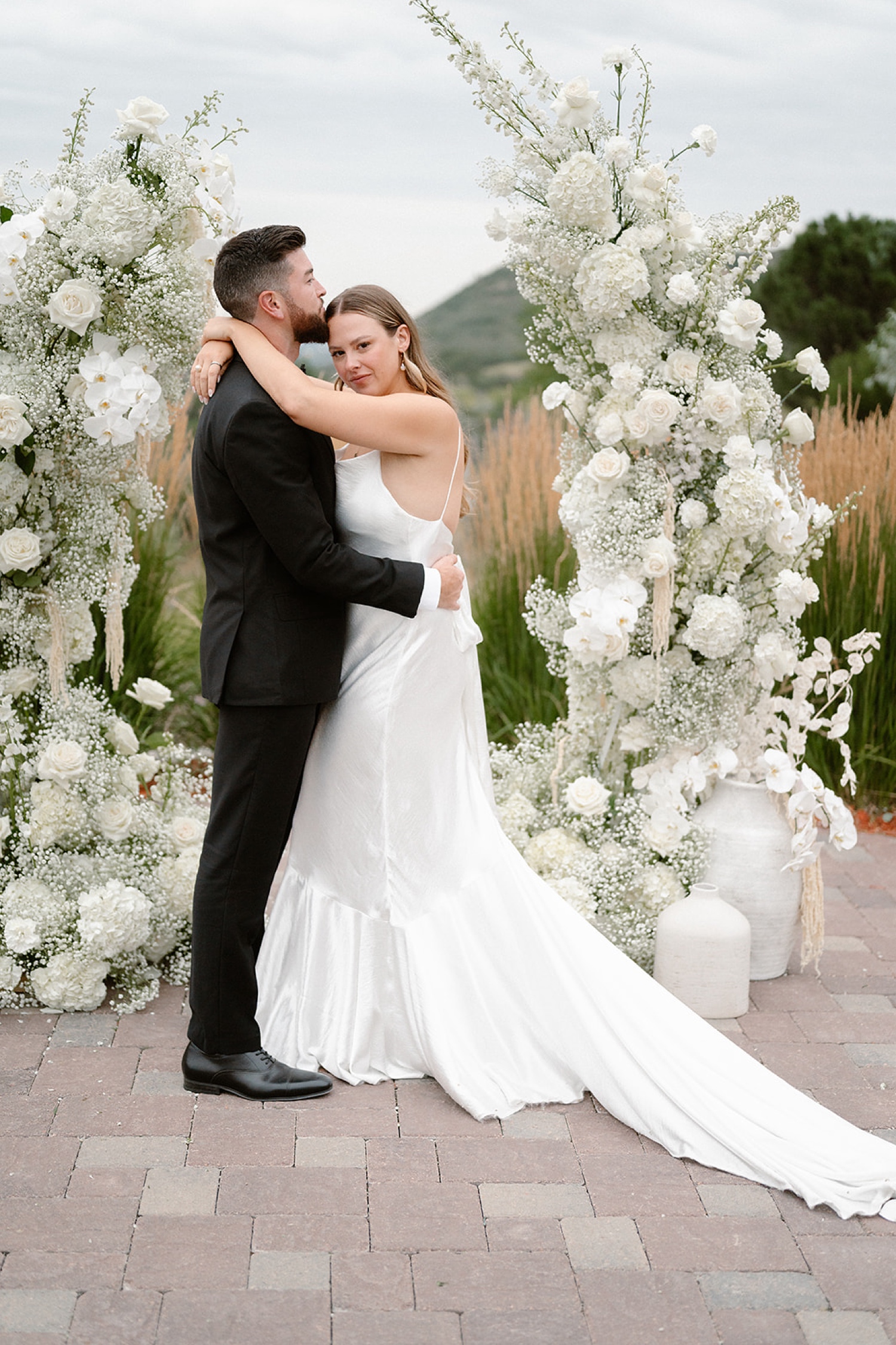 A bride and groom embrace for their wedding portraits in front of their wedding arch