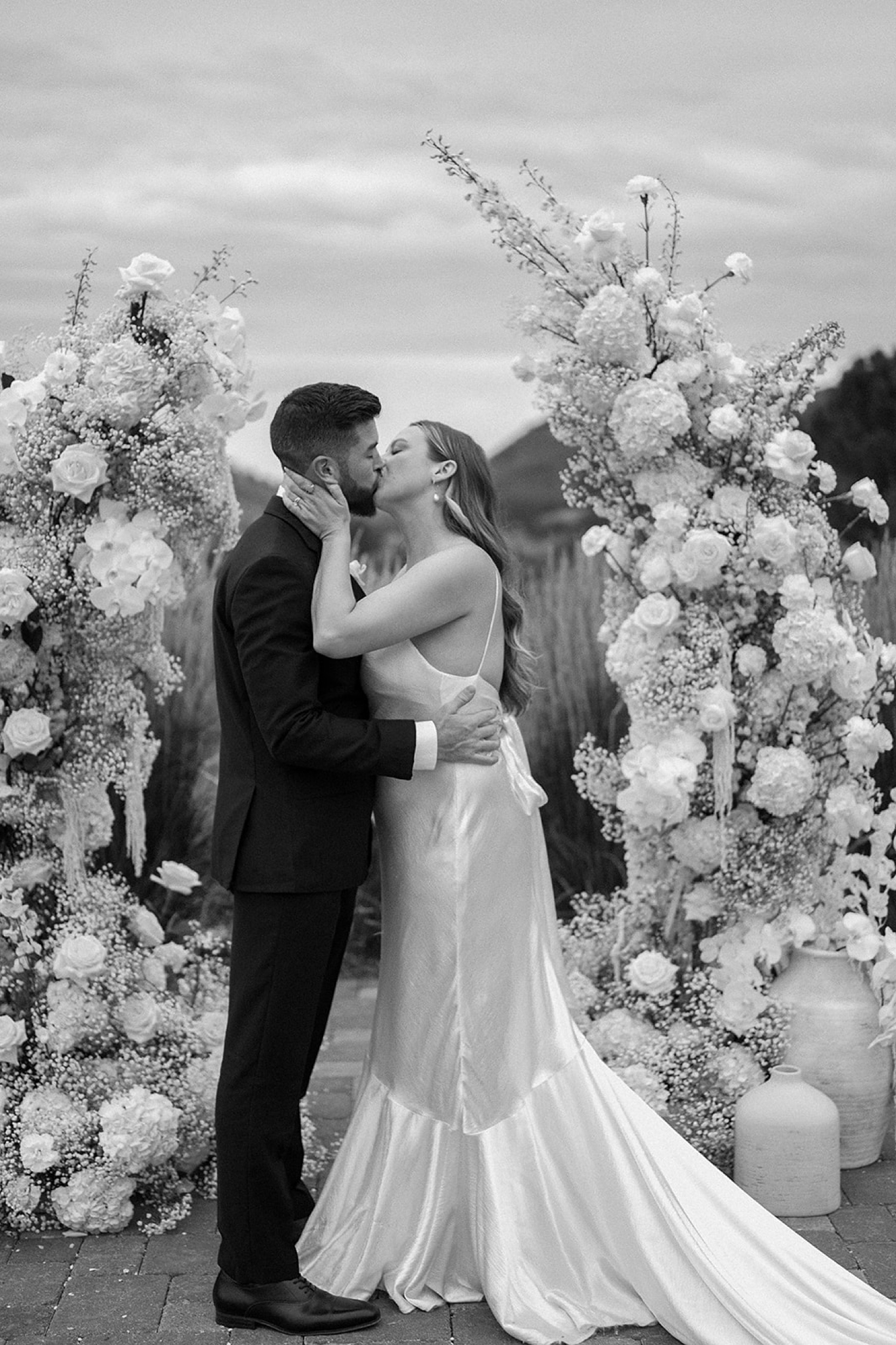 A bride and groom kissing one another in front of their wedding arch