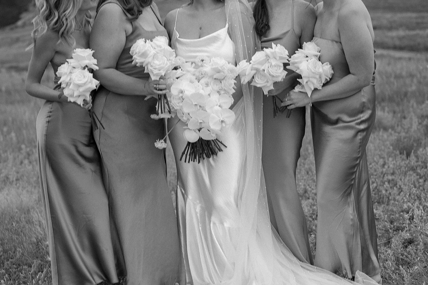 A bride and her bridesmaids stand together while they hold their wedding bouquets in front of them