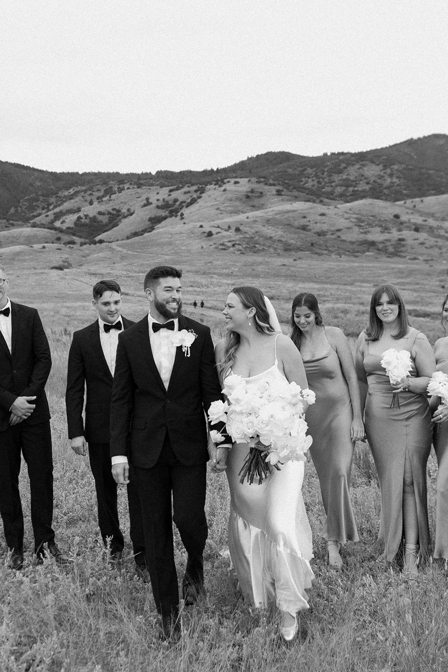 A bride and groom walk towards the camera with their wedding party following behind