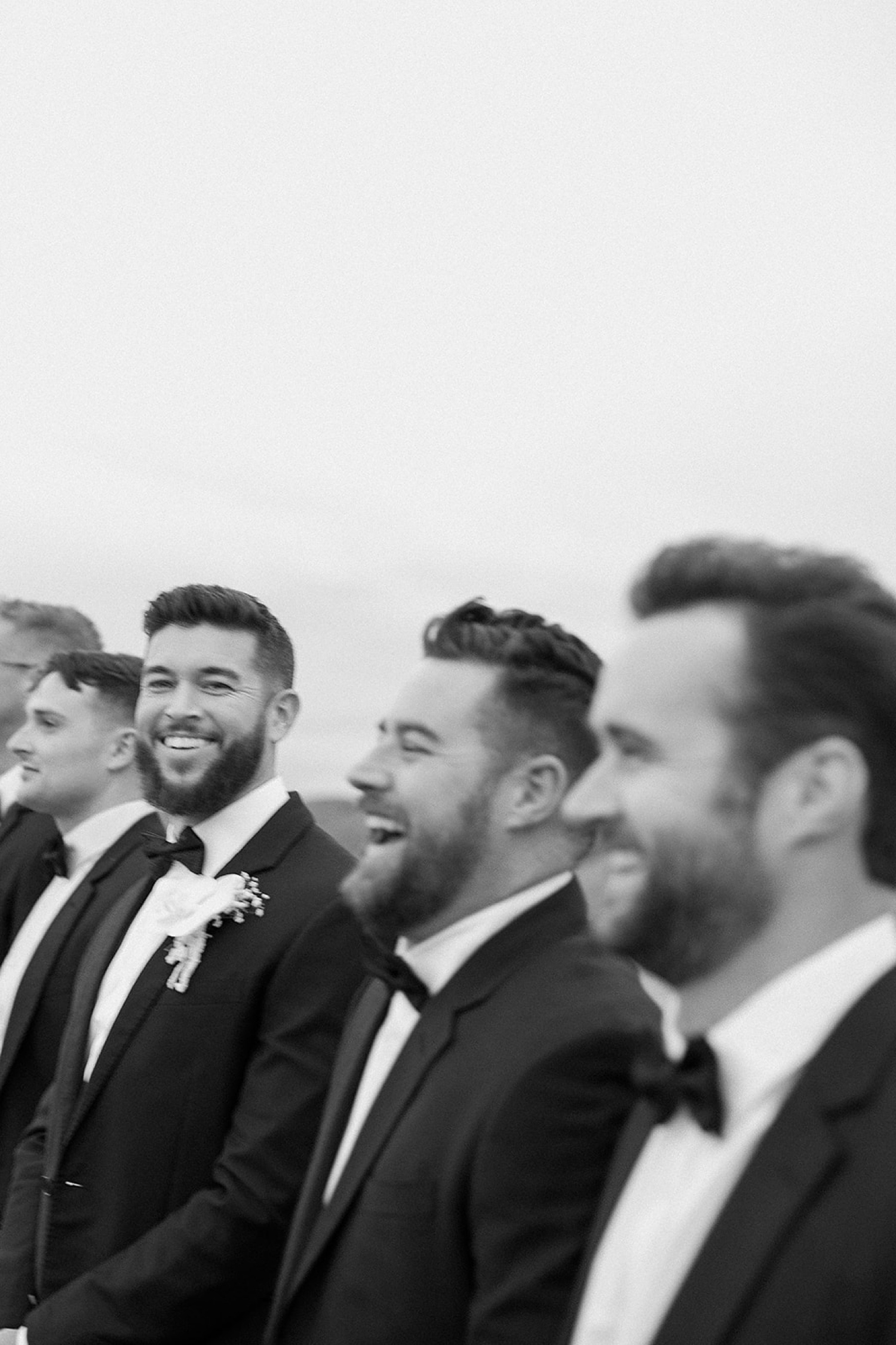 A groom stands with his groomsmen while they all laugh together