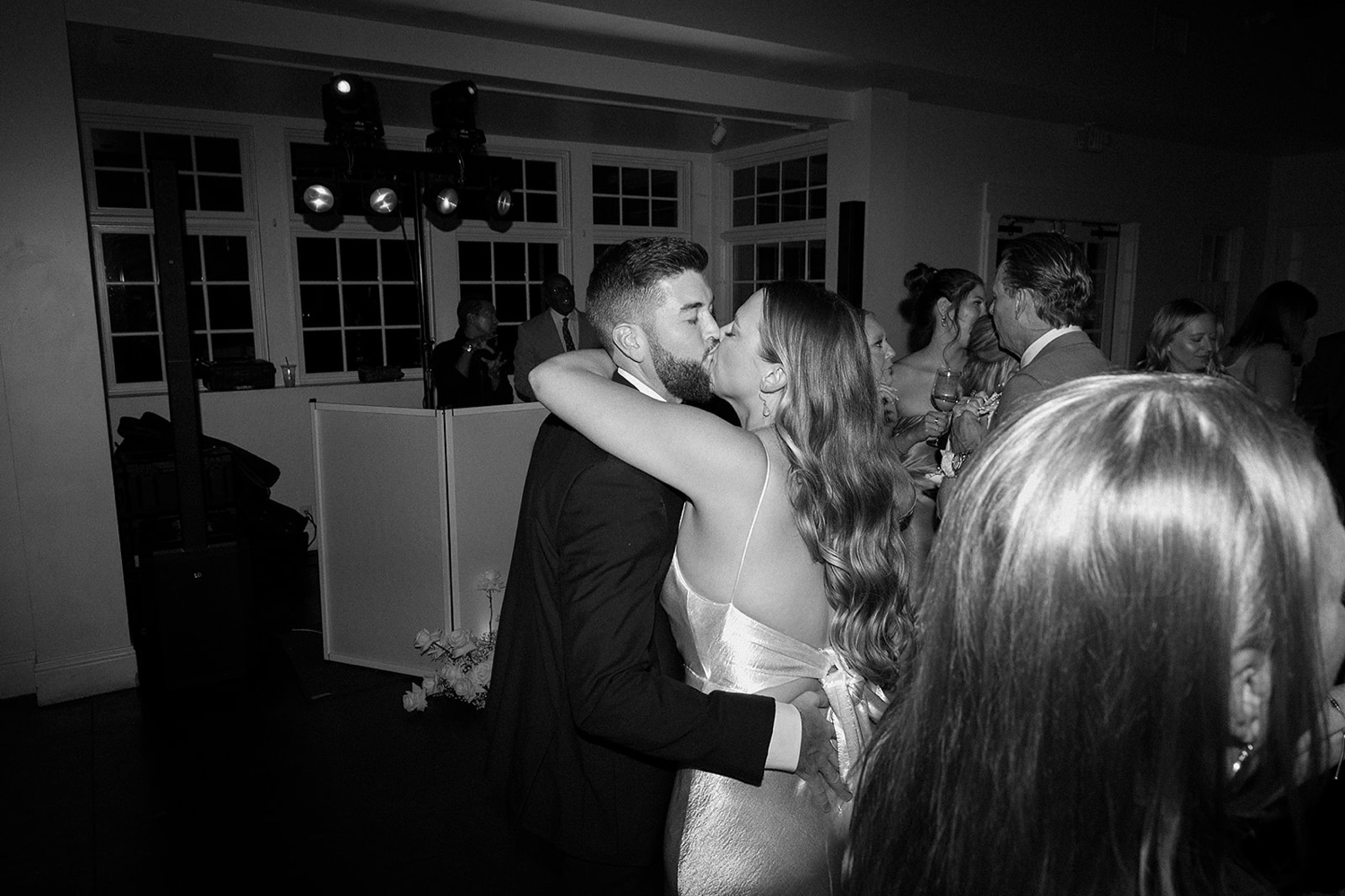 A bride and groom dance and kiss one another on the wedding dance floor while their surrounded by their wedding guests