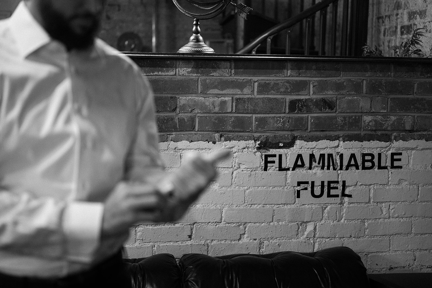 Groom getting dressed with "Flammable Fuel" written on a brick wall in the background