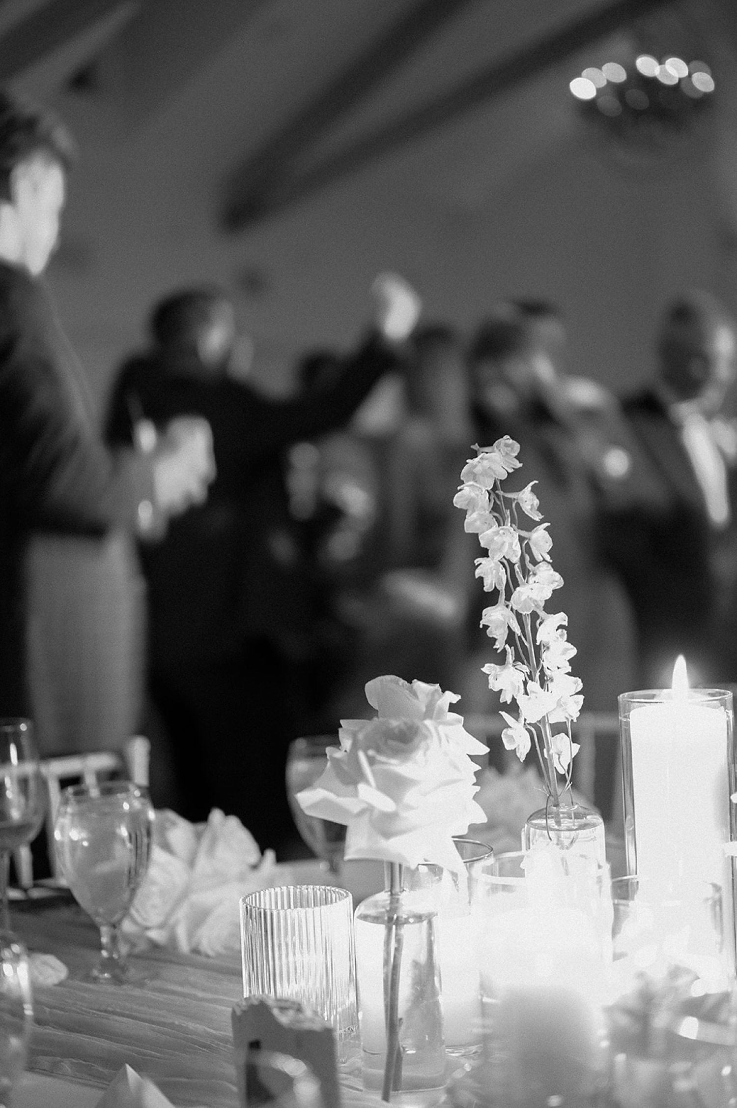 Wedding flowers and candles on a table with wedding guests dancing in the background