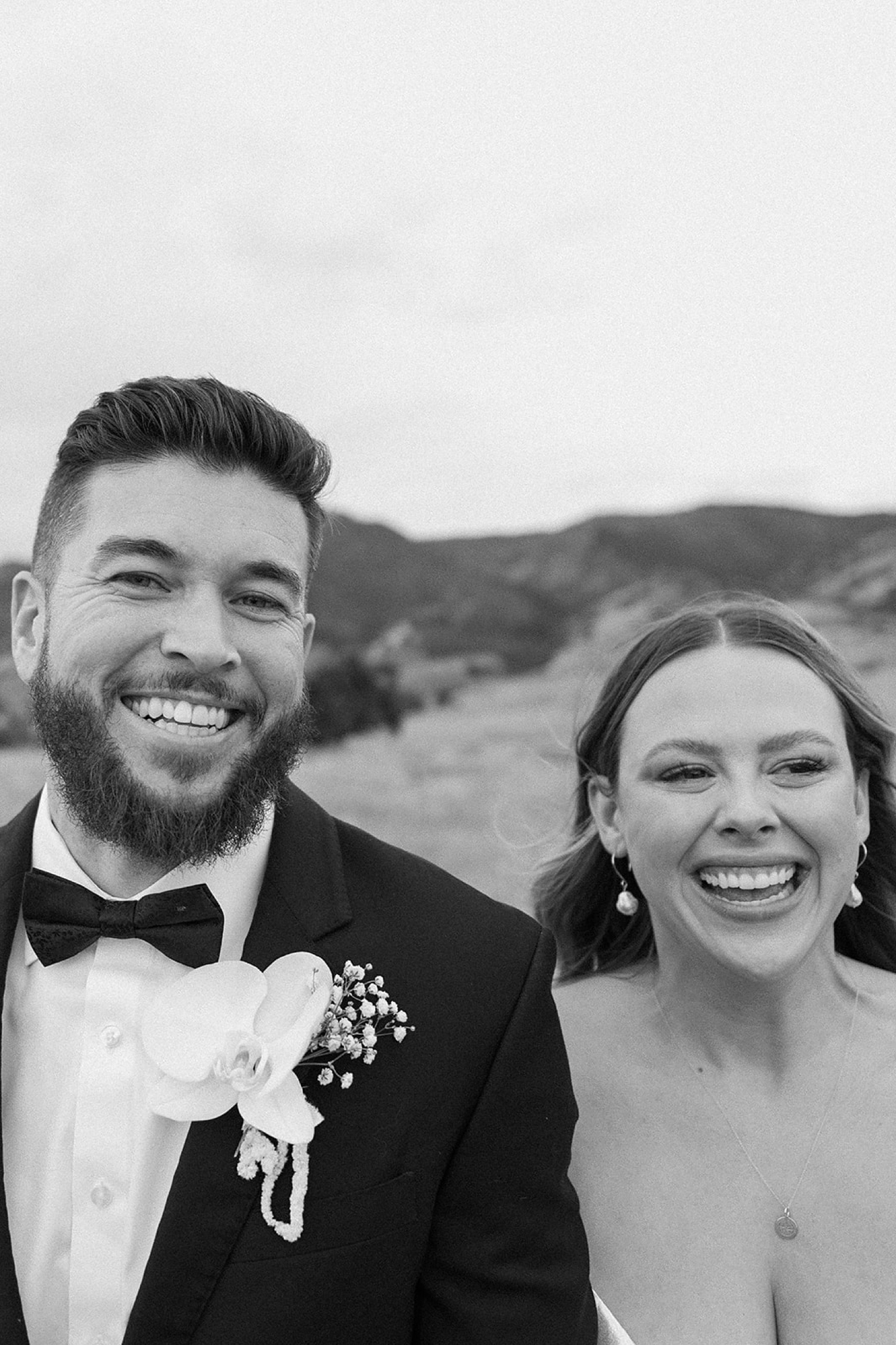 A bride and groom smile at the camera while they walk towards the camera for their wedding portraits at The Manor House