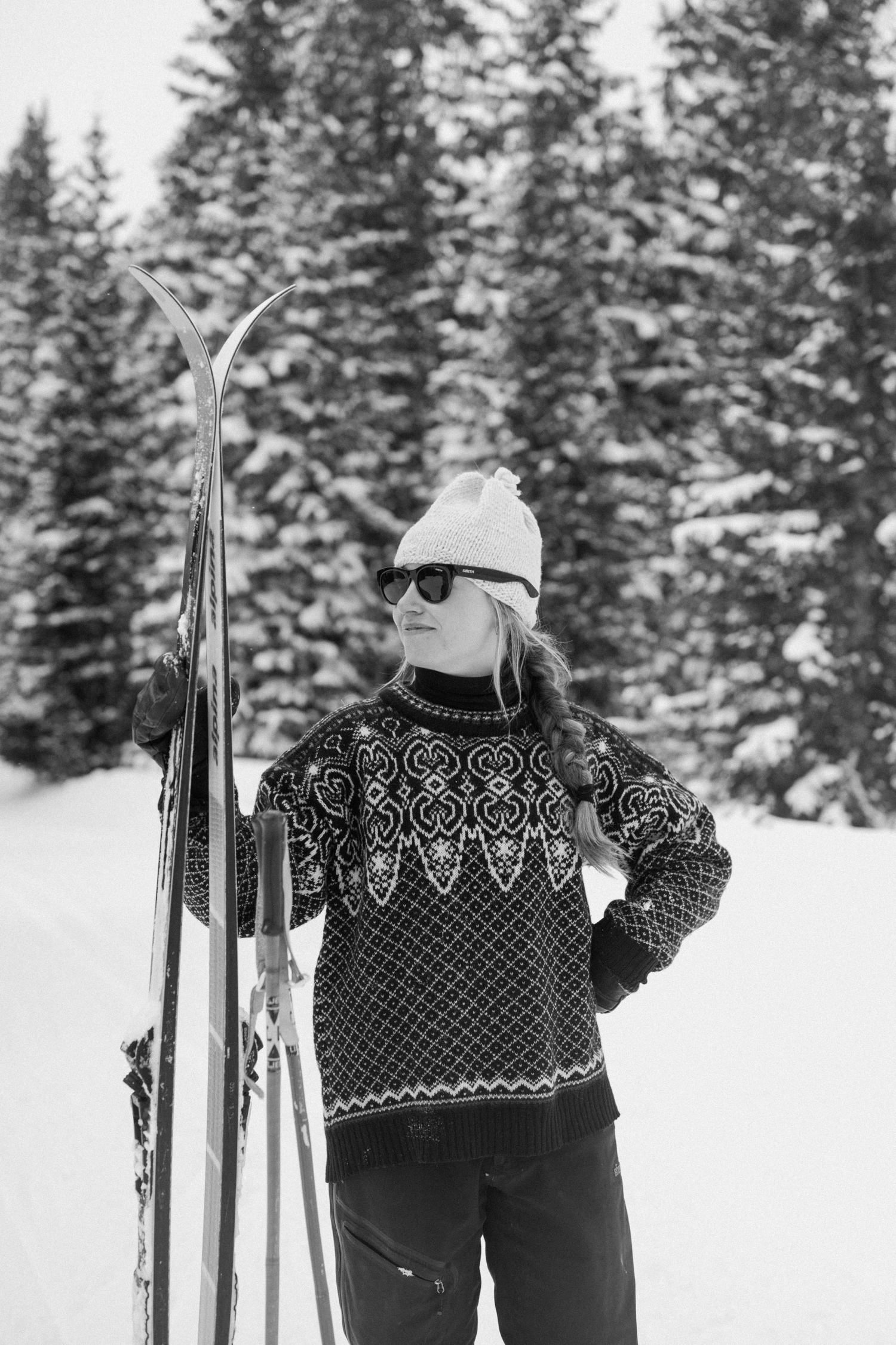 Bride-to-be in stylish winter coat and hat, smiling during her winter engagement photo session with her fiancé in the snow-covered Colorado mountains.