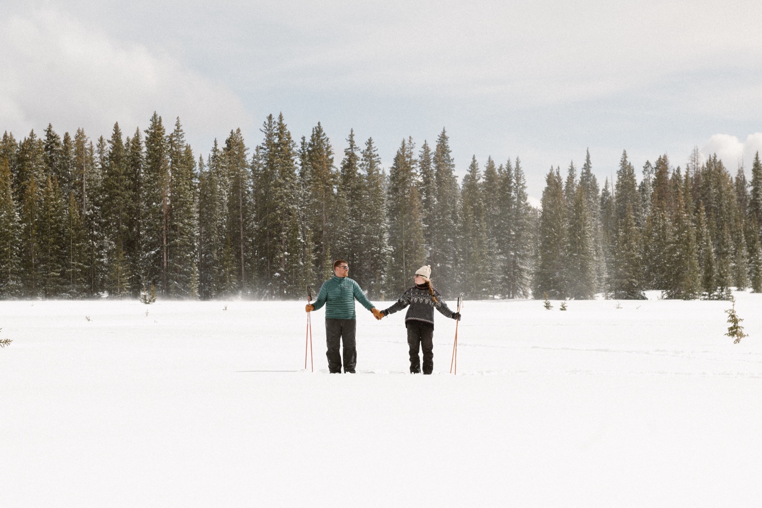 Bride and groom-to-be holding hands and walking through snowy trails during their winter engagement session in the mountains of Montrose, Colorado.