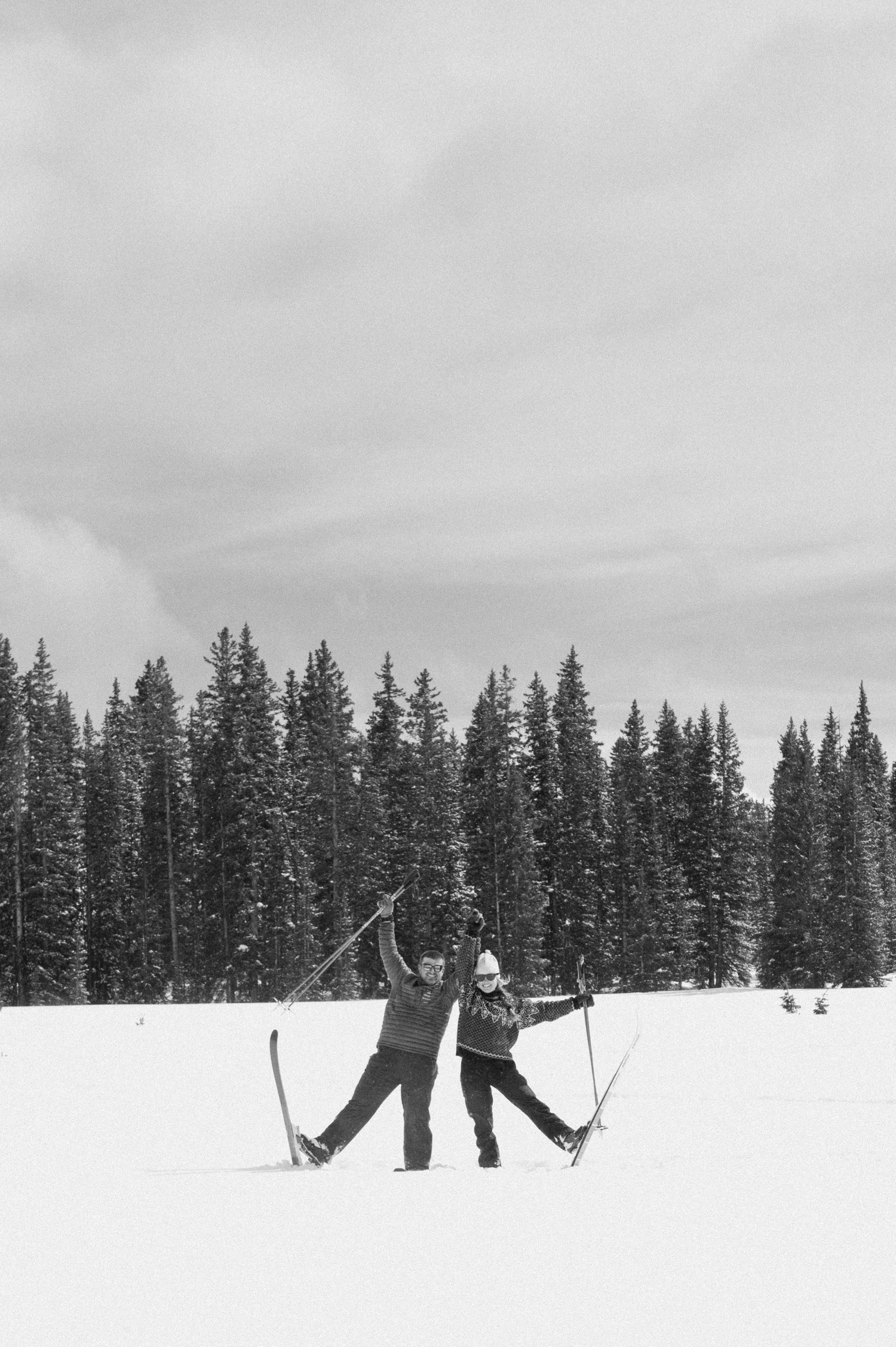 A couple laughing together while bundled up in cozy coats during their winter engagement photo session on cross-country skis in Montrose, Colorado.