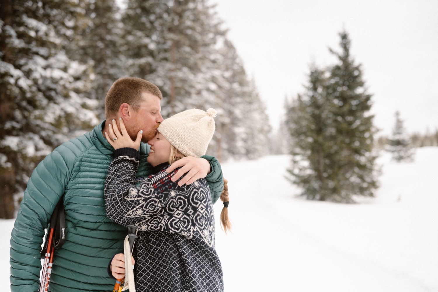 Couple cuddling in snowy forest during winter engagement photos session in Montrose, Colorado, with beautiful winter landscape in the background.