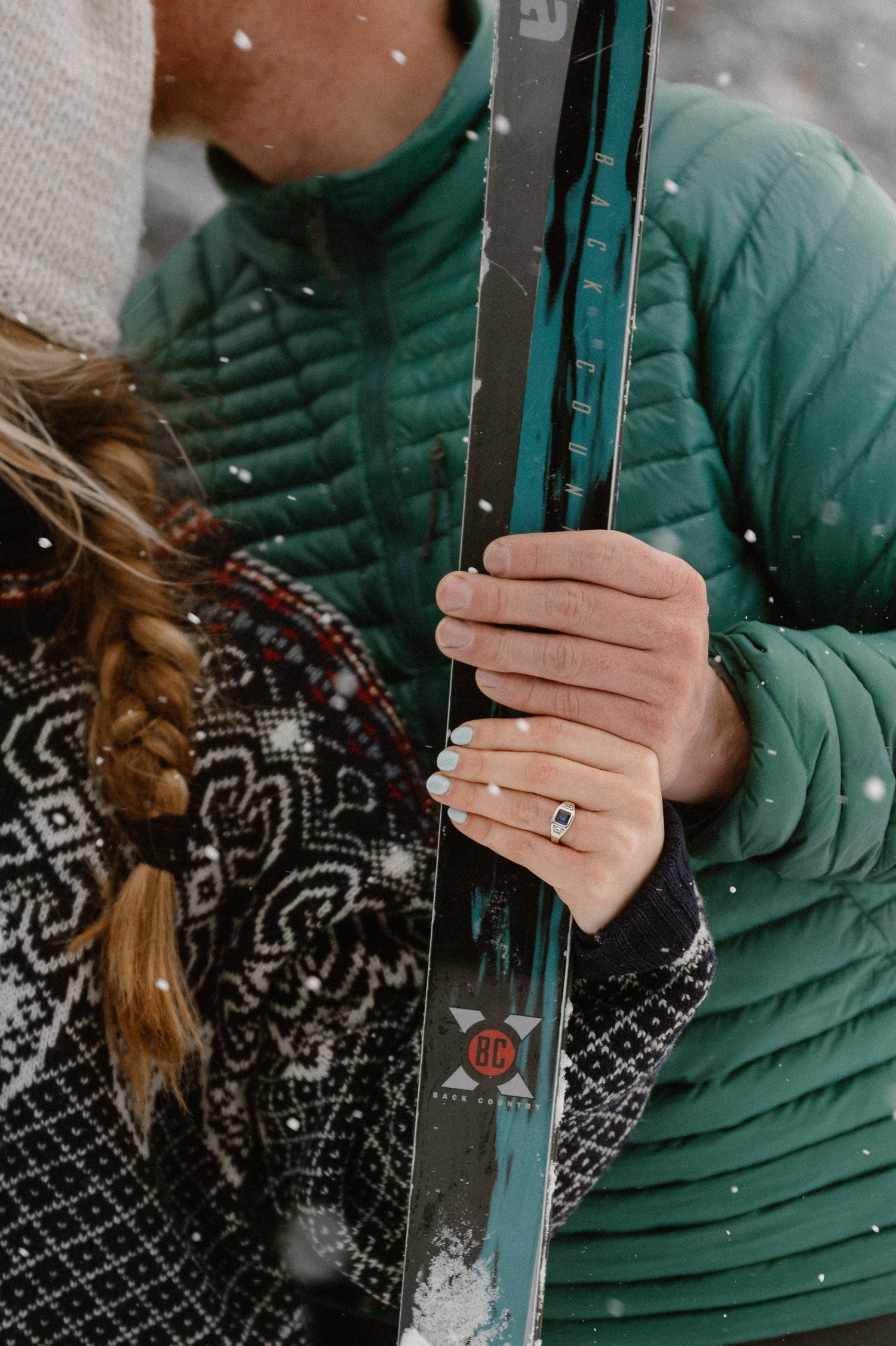 Couple stops for a photo break while cross-country skiing, with snow-covered mountains and winter engagement outfits in the background.