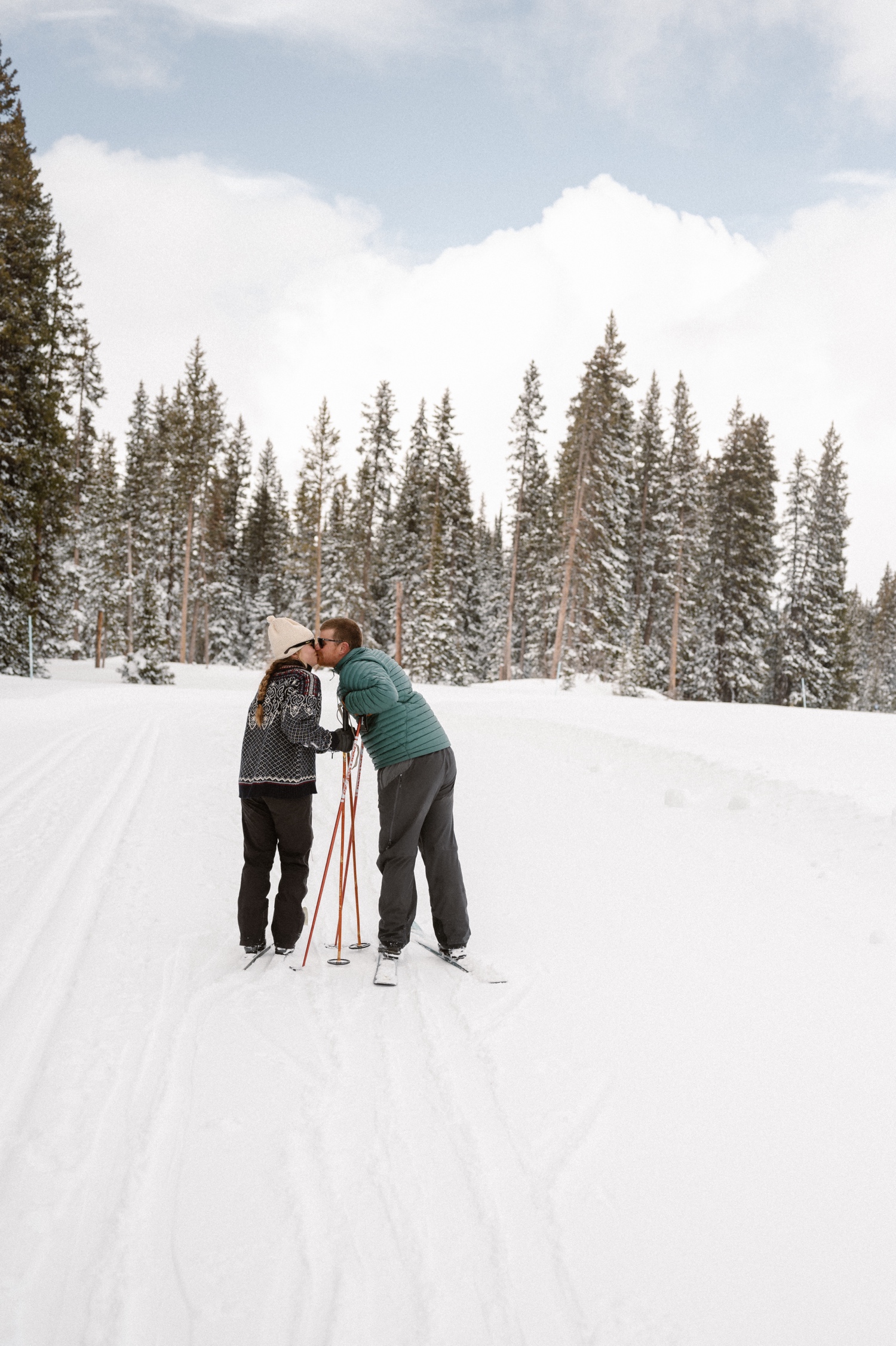 A couple laughing together while bundled up in cozy coats during their winter engagement photo session on cross-country skis in Montrose, Colorado.