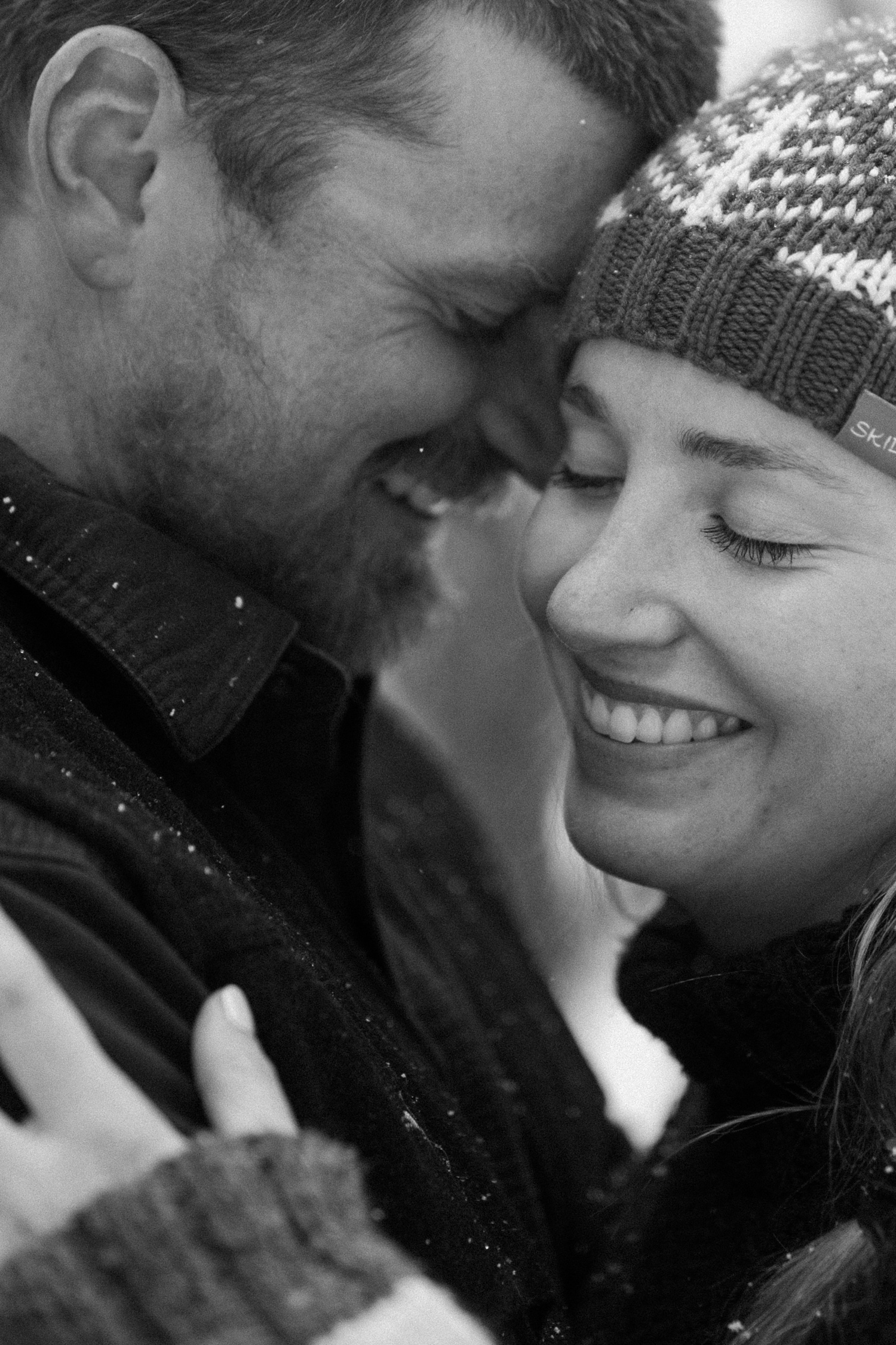 A couple laughing together while bundled up in cozy coats during their winter engagement photo session on cross-country skis in Montrose, Colorado.