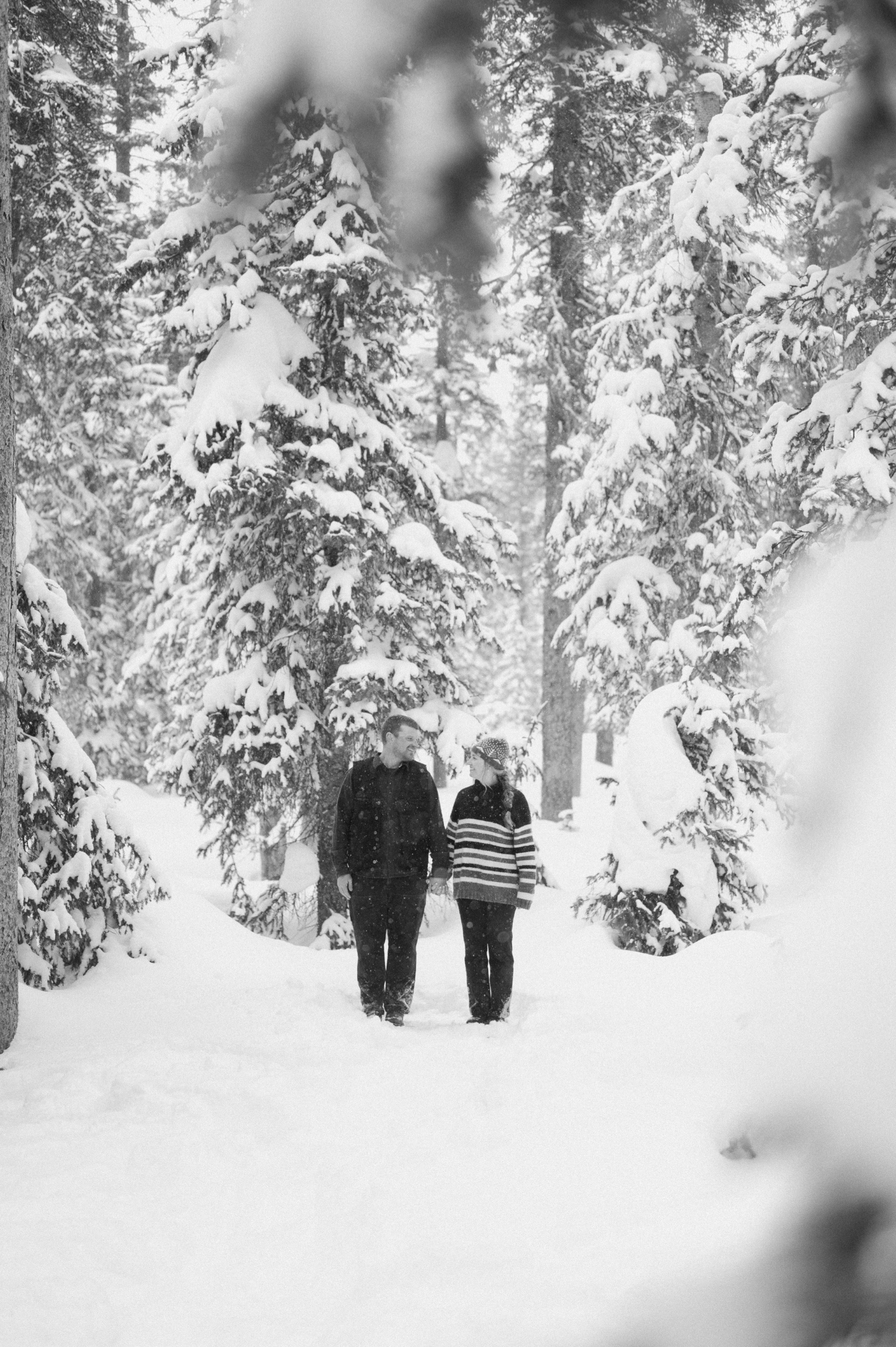 Couple stops for a photo break while cross-country skiing, with snow-covered mountains and winter engagement outfits in the background.