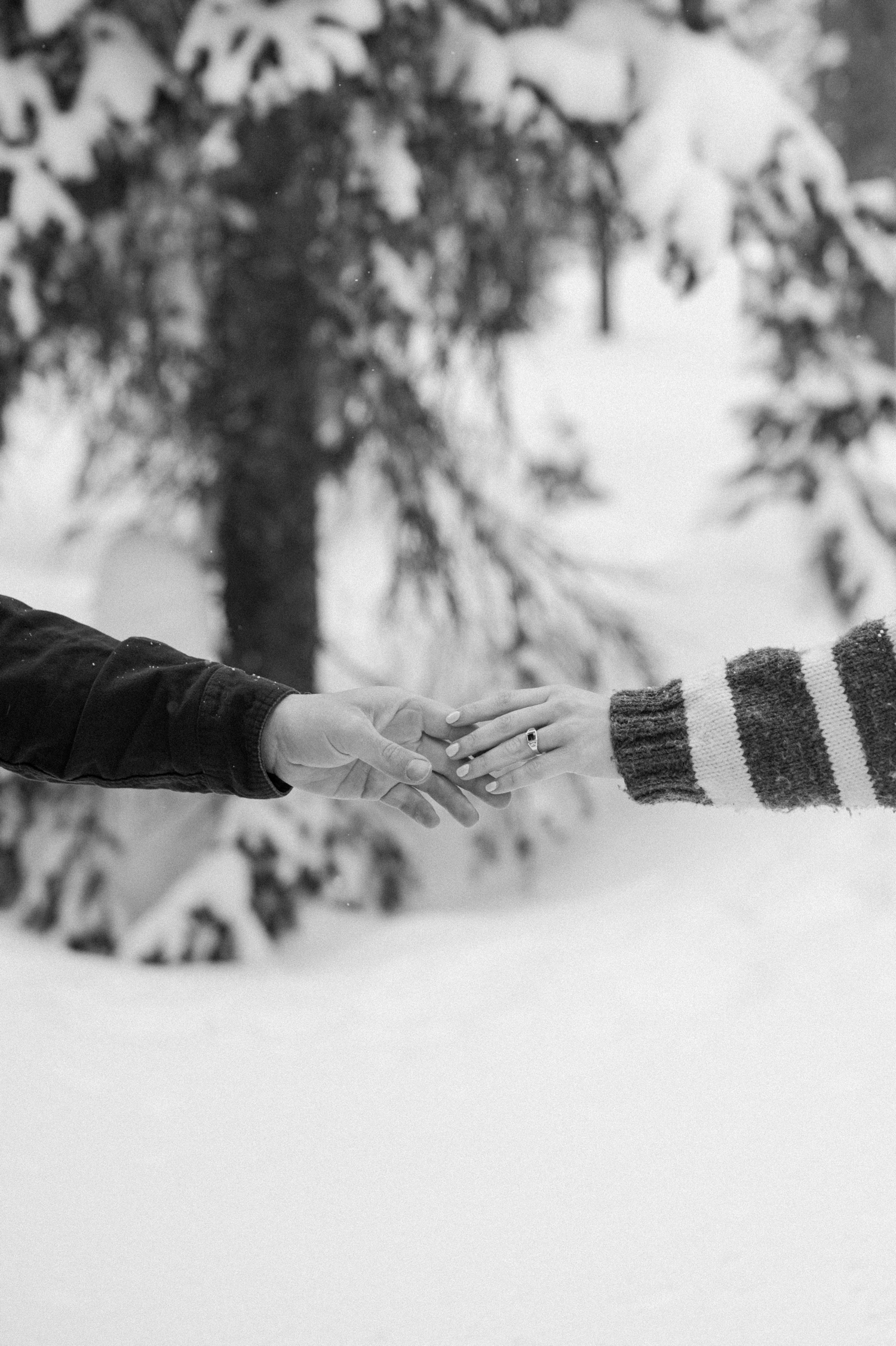 Couple stops for a photo break while cross-country skiing, with snow-covered mountains and winter engagement outfits in the background.