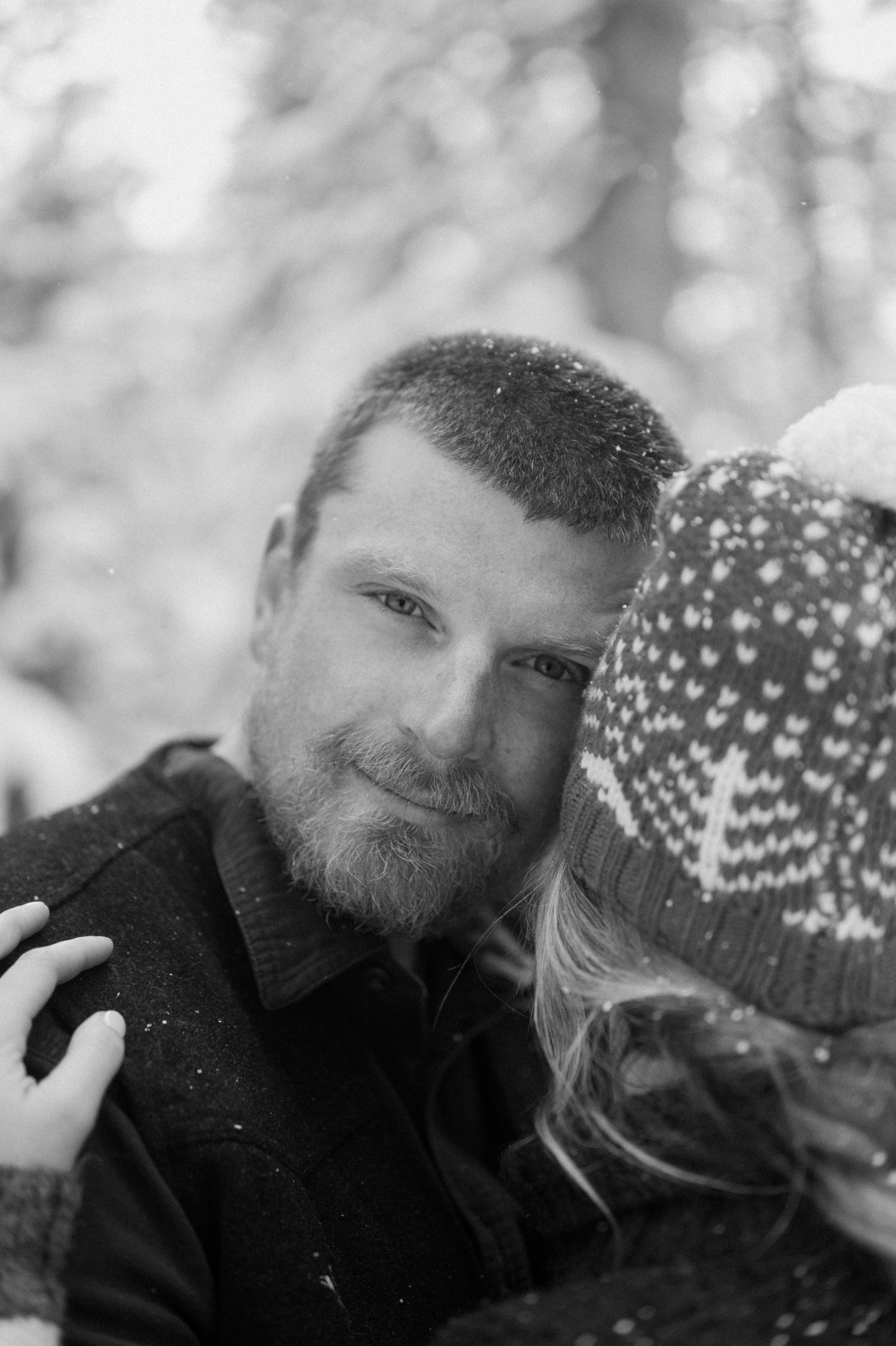 Couple stops for a photo break while cross-country skiing, with snow-covered mountains and winter engagement outfits in the background.