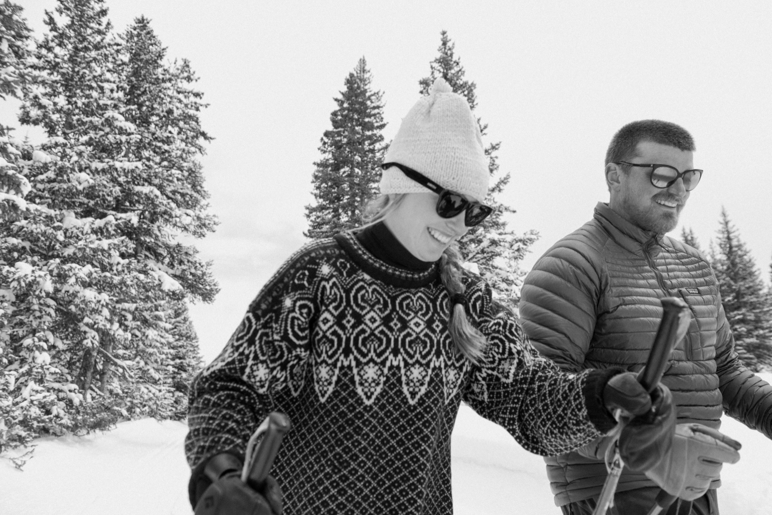 Couple cross-country skiing in snowy forest, wearing winter engagement outfits, during their winter engagement session near Montrose, Colorado.