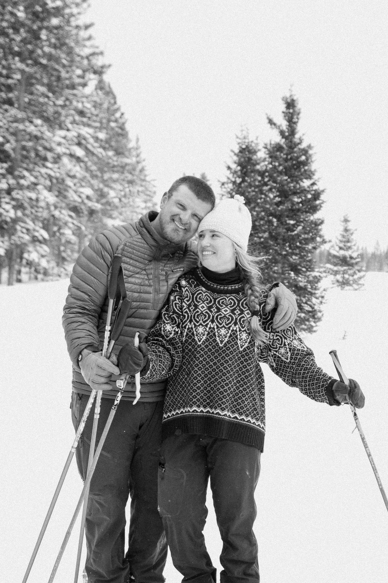 Couple cross-country skiing in snowy forest, wearing winter engagement outfits, during their winter engagement session near Montrose, Colorado.