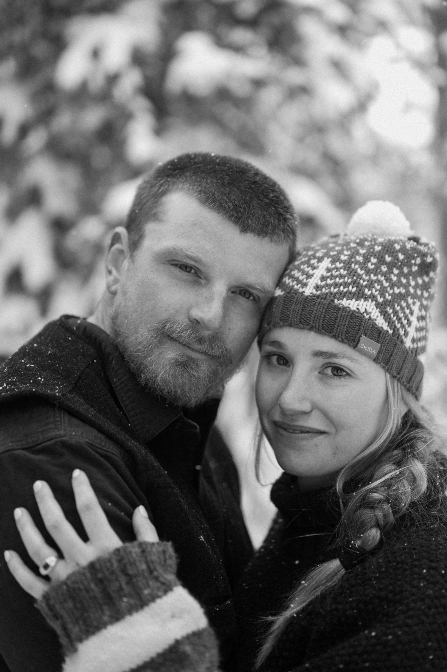 Couple cross-country skiing in snowy forest, wearing winter engagement outfits, during their winter engagement session near Montrose, Colorado.