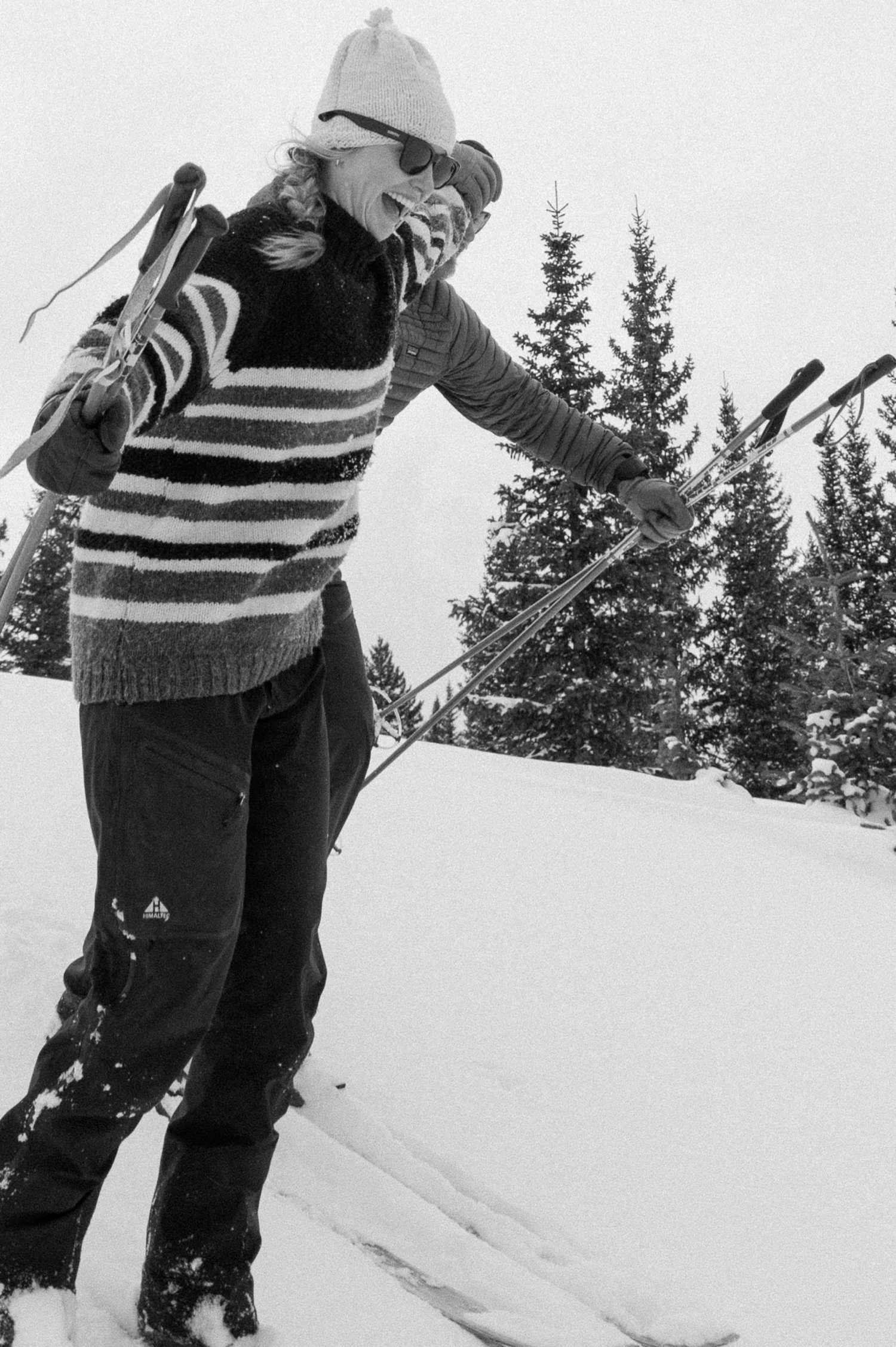 Couple cross-country skiing in snowy forest, wearing winter engagement outfits, during their winter engagement session near Montrose, Colorado.