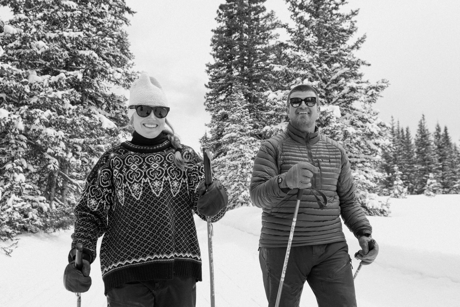 Bride-to-be in stylish winter coat and hat, smiling during her winter engagement photo session with her fiancé in the snow-covered Colorado mountains.